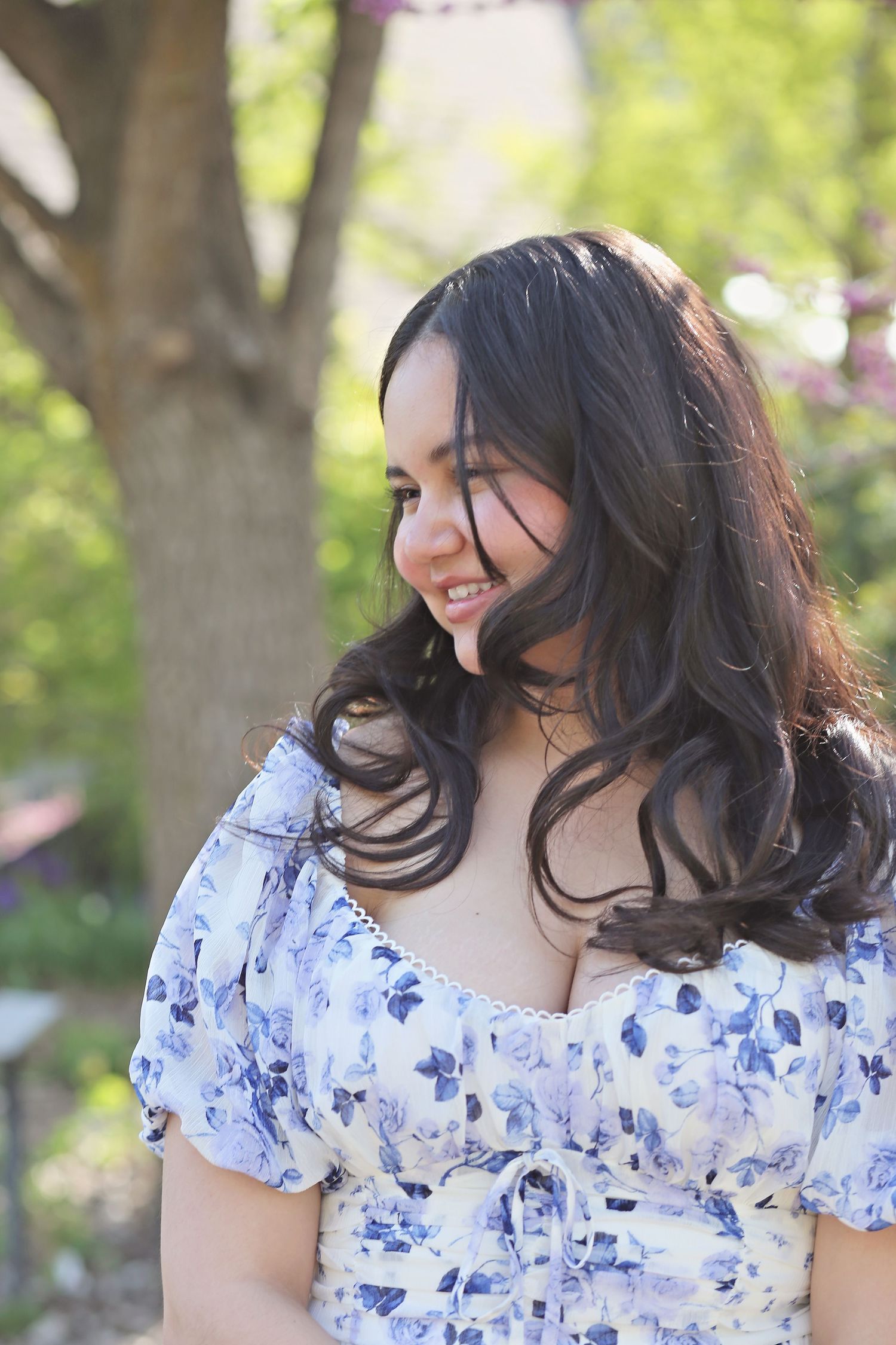 Graduate wearing floral dress poses in natural outdoor setting.