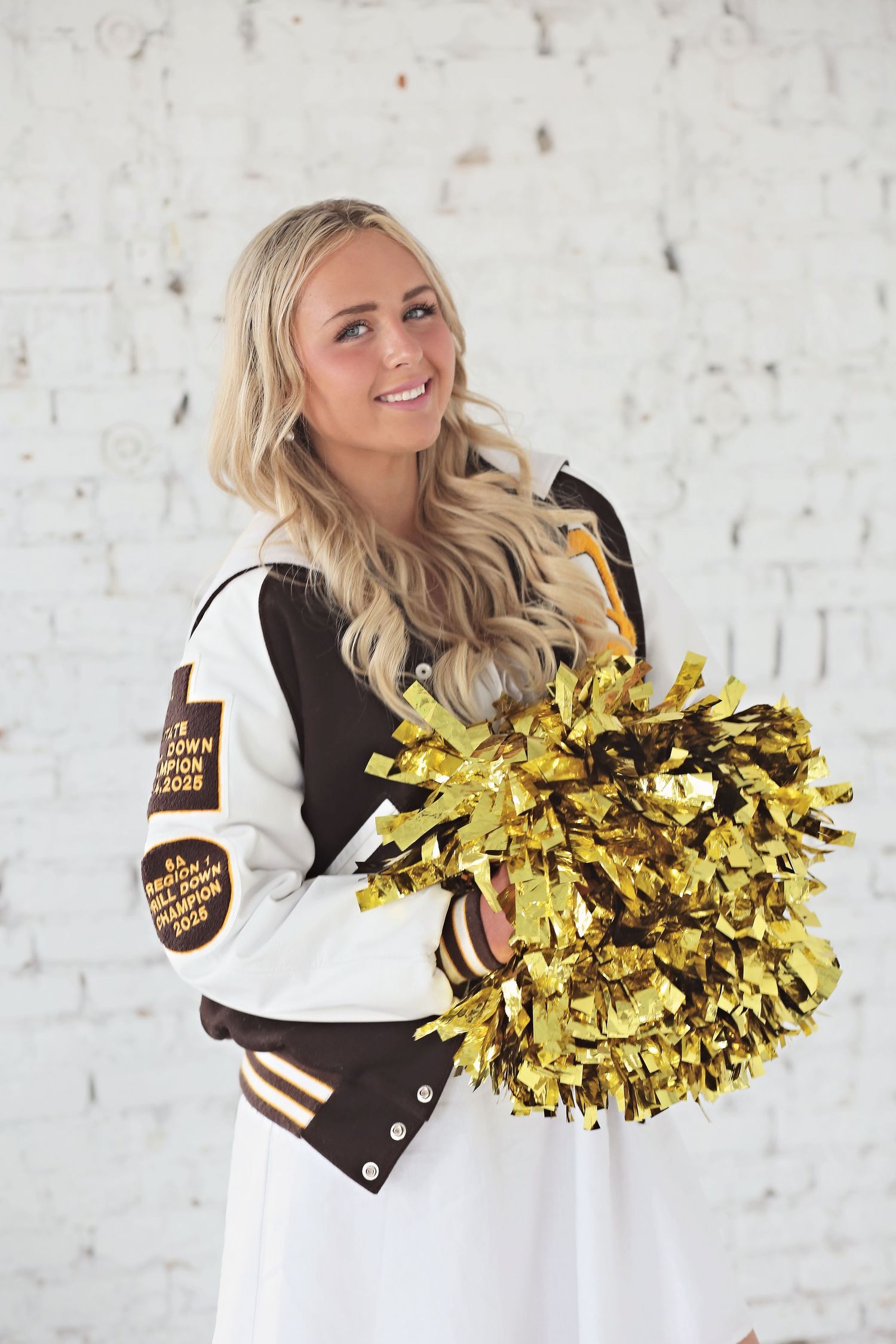Cheerleader in black and white uniform holds gold pom poms against white brick wall in three dynamic poses.
