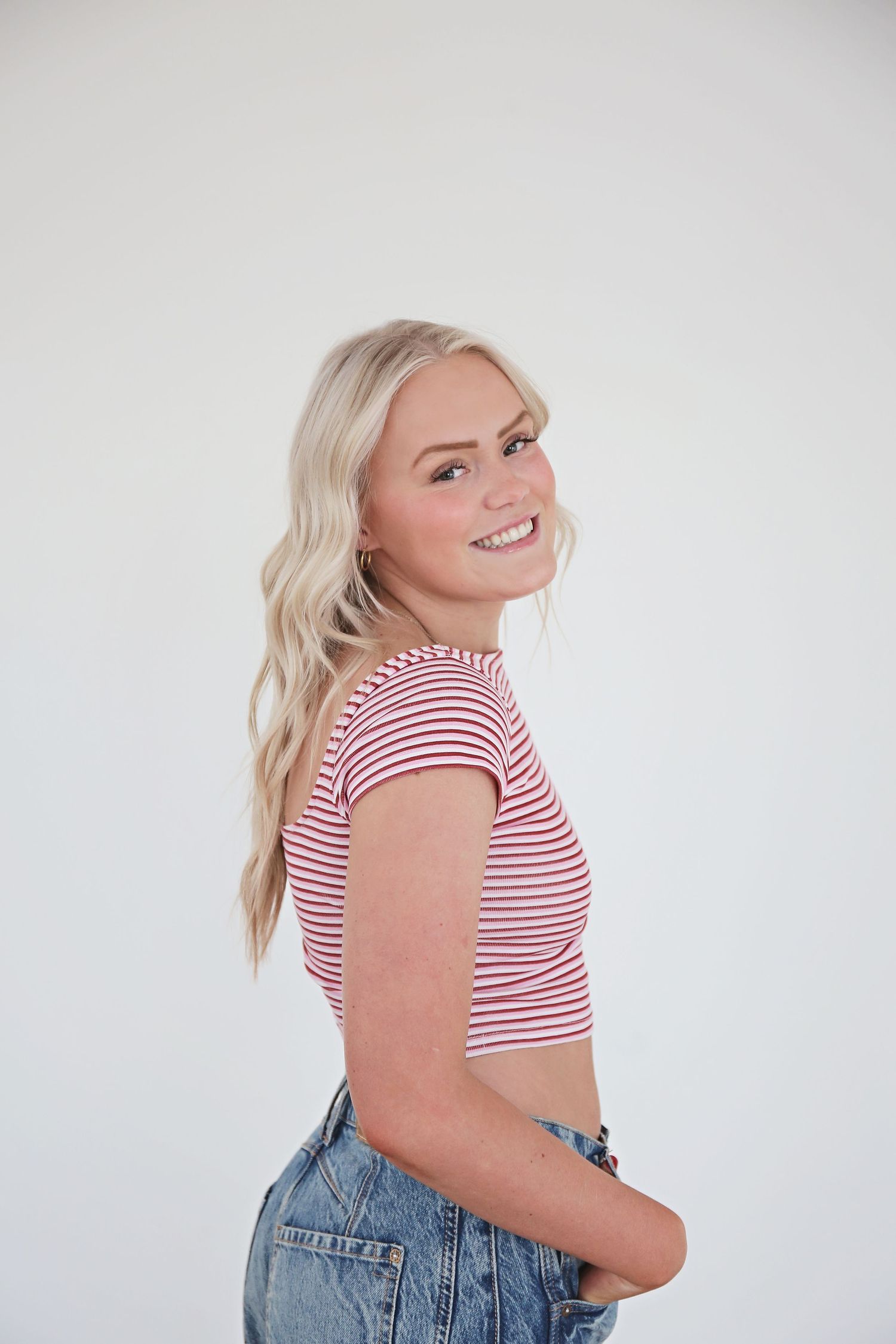 Person in striped top and denim poses against white background in studio setting.