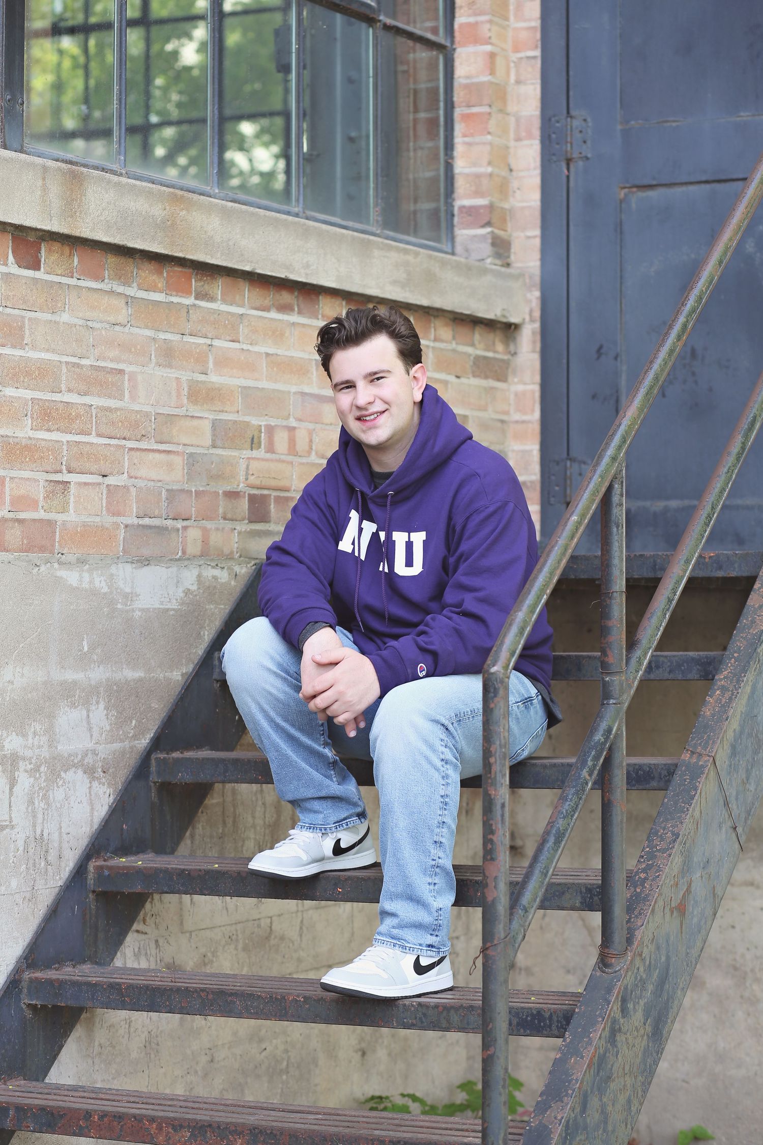 Student in purple university hoodie sitting on industrial metal stairs.