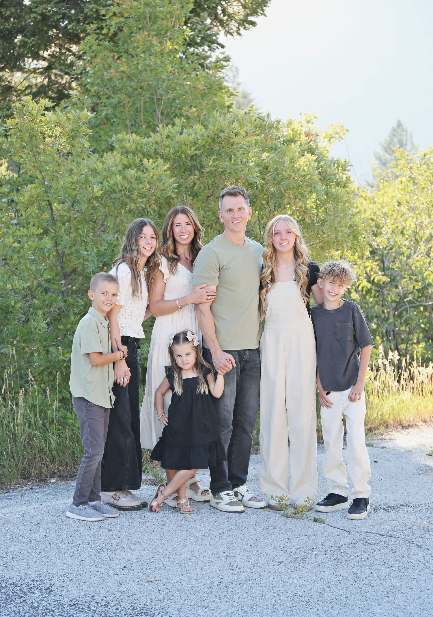 Family group poses together on light gravel path with green foliage in background.