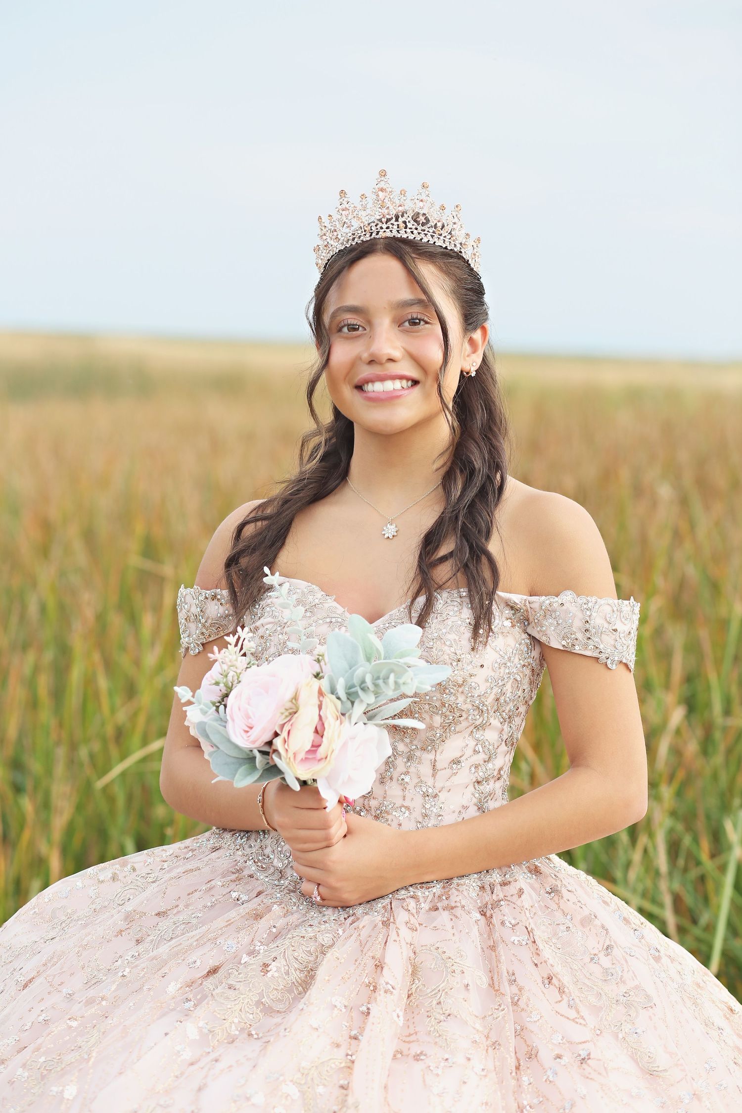 Stunning pink princess gown with off-shoulder design and tiara photographed in field setting.