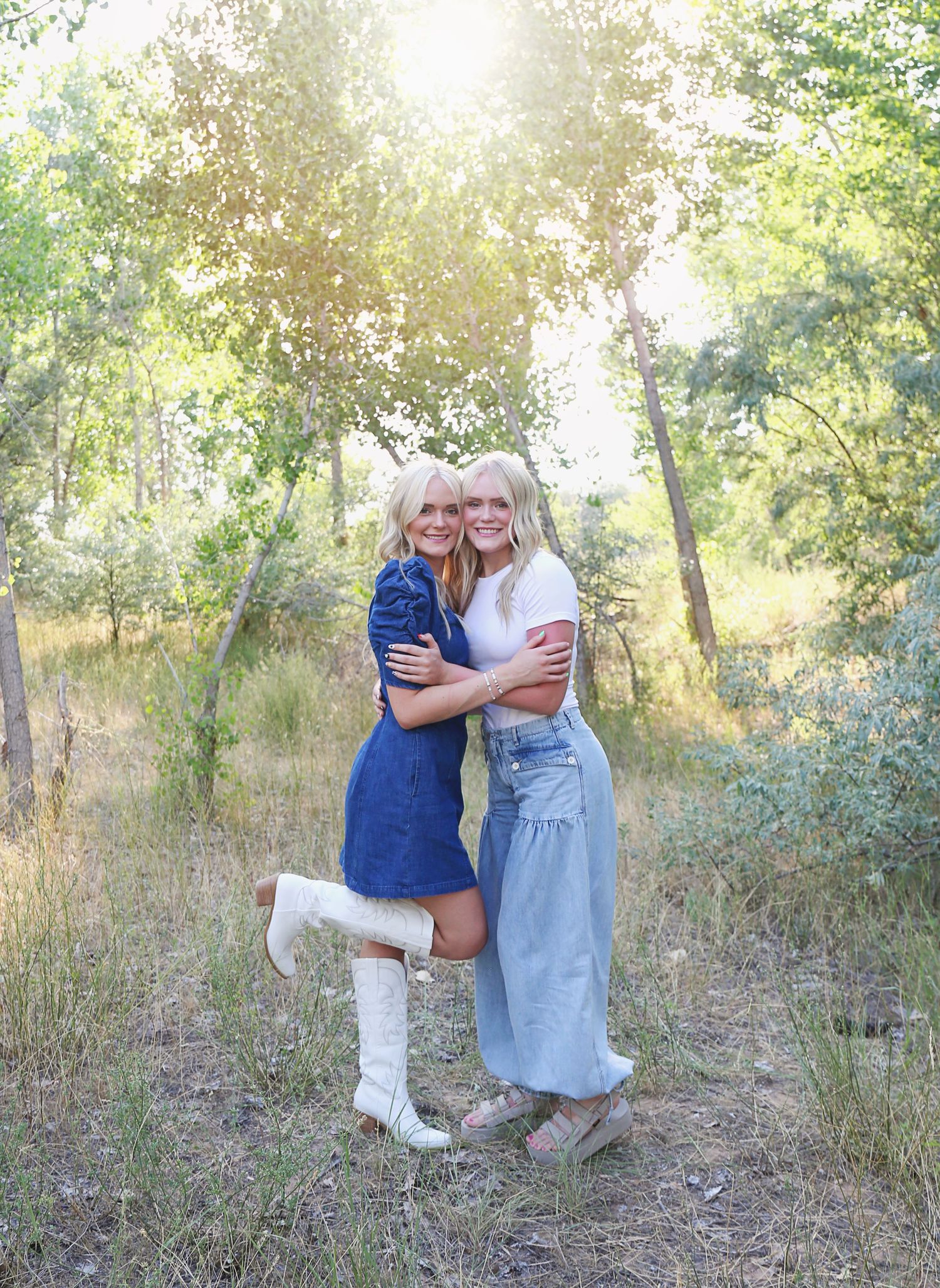 Two friends sharing a joyful embrace in a sunlit wooded area.