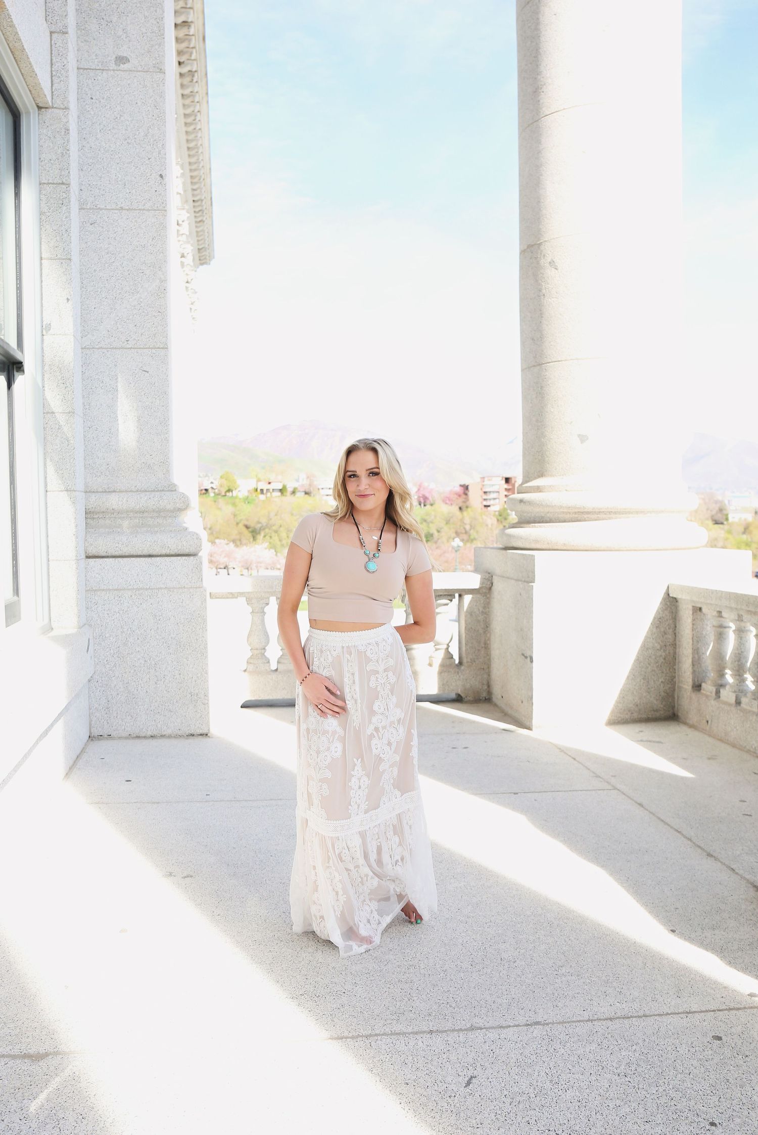 Person in flowing white dress posing in bright sunlit colonnade.