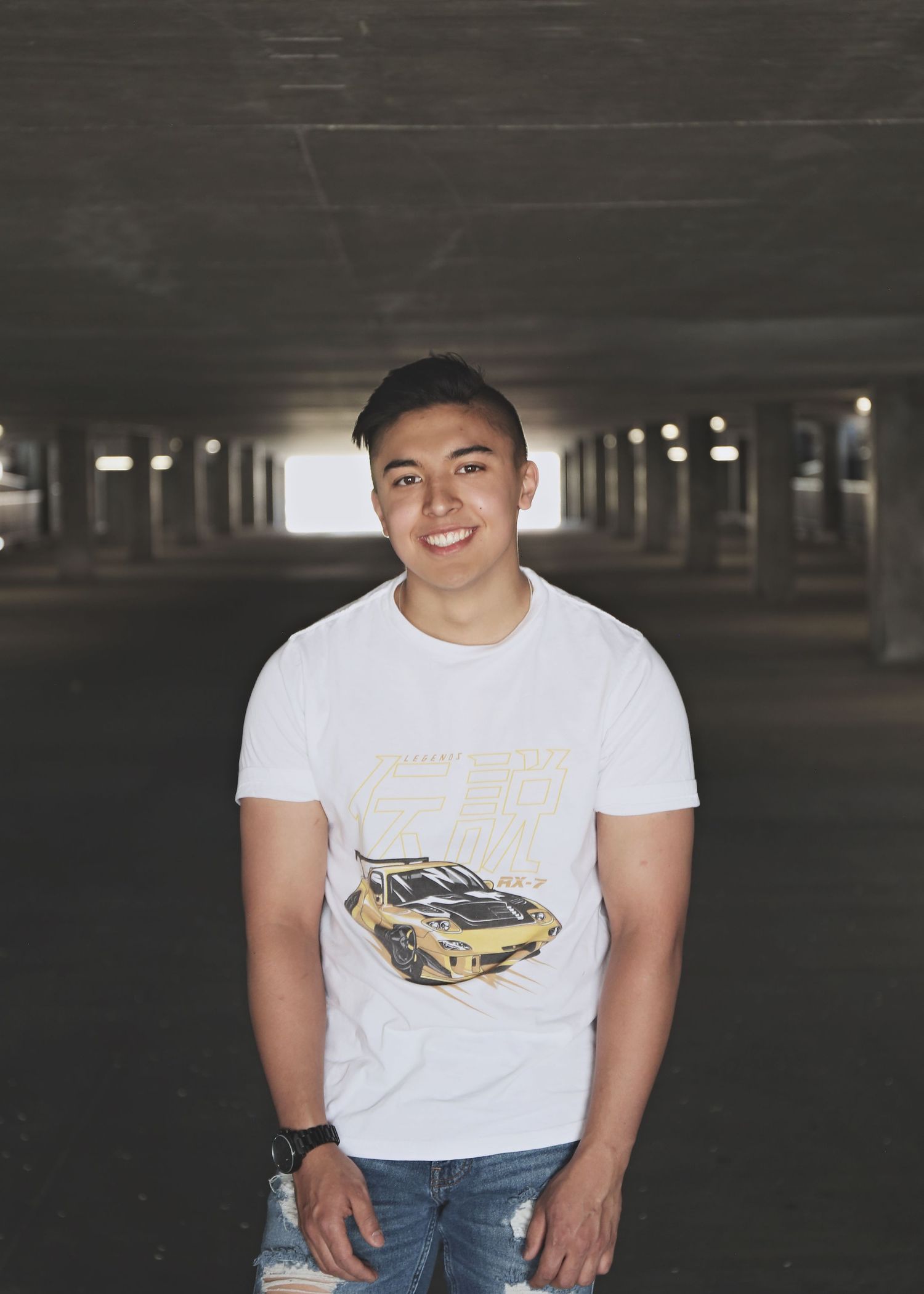 Person wearing white t-shirt with car graphic posing in parking garage.