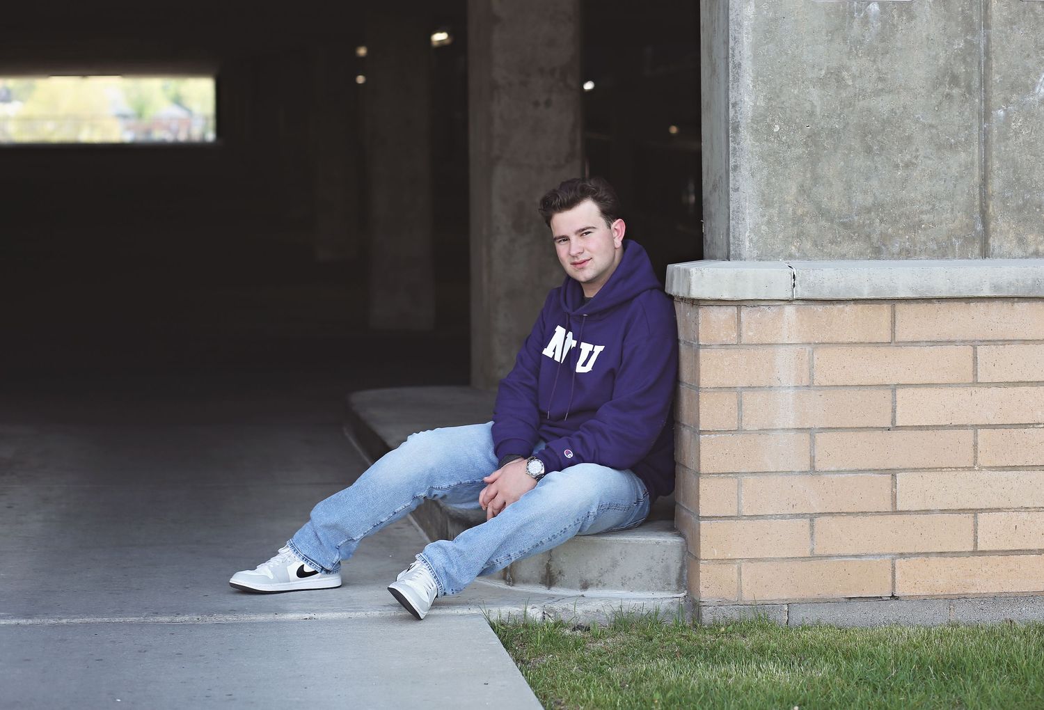 Casual portrait of person sitting on concrete ledge wearing purple hoodie and jeans.