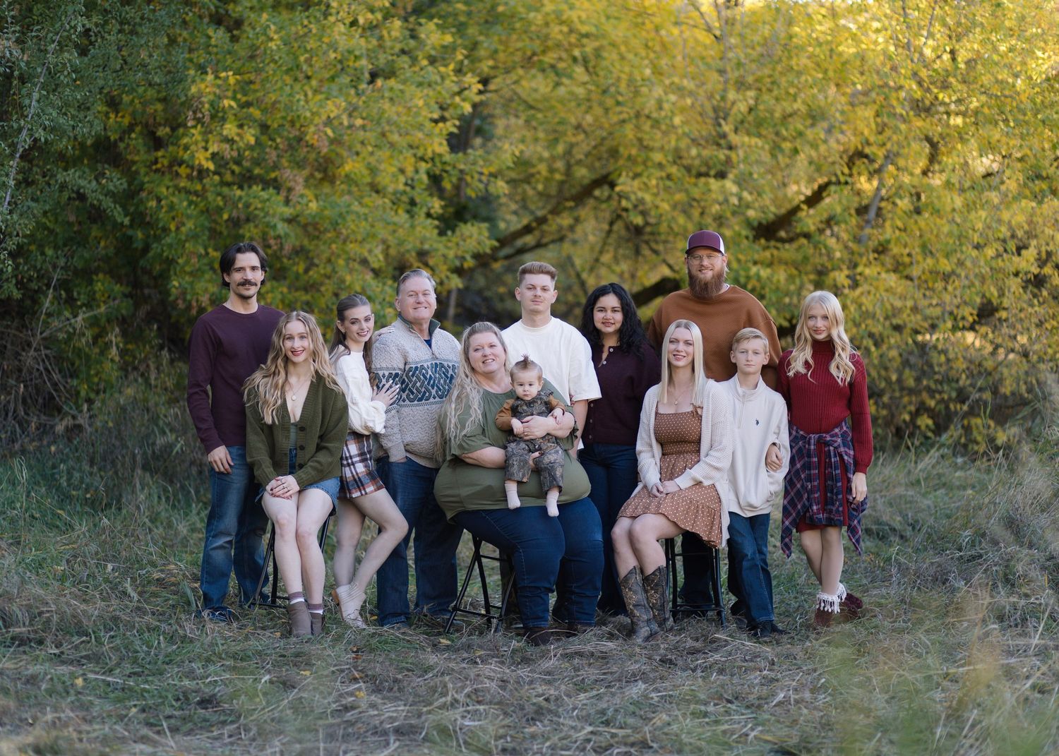 Large extended family gathering for outdoor portraits against a backdrop of yellow autumn leaves.