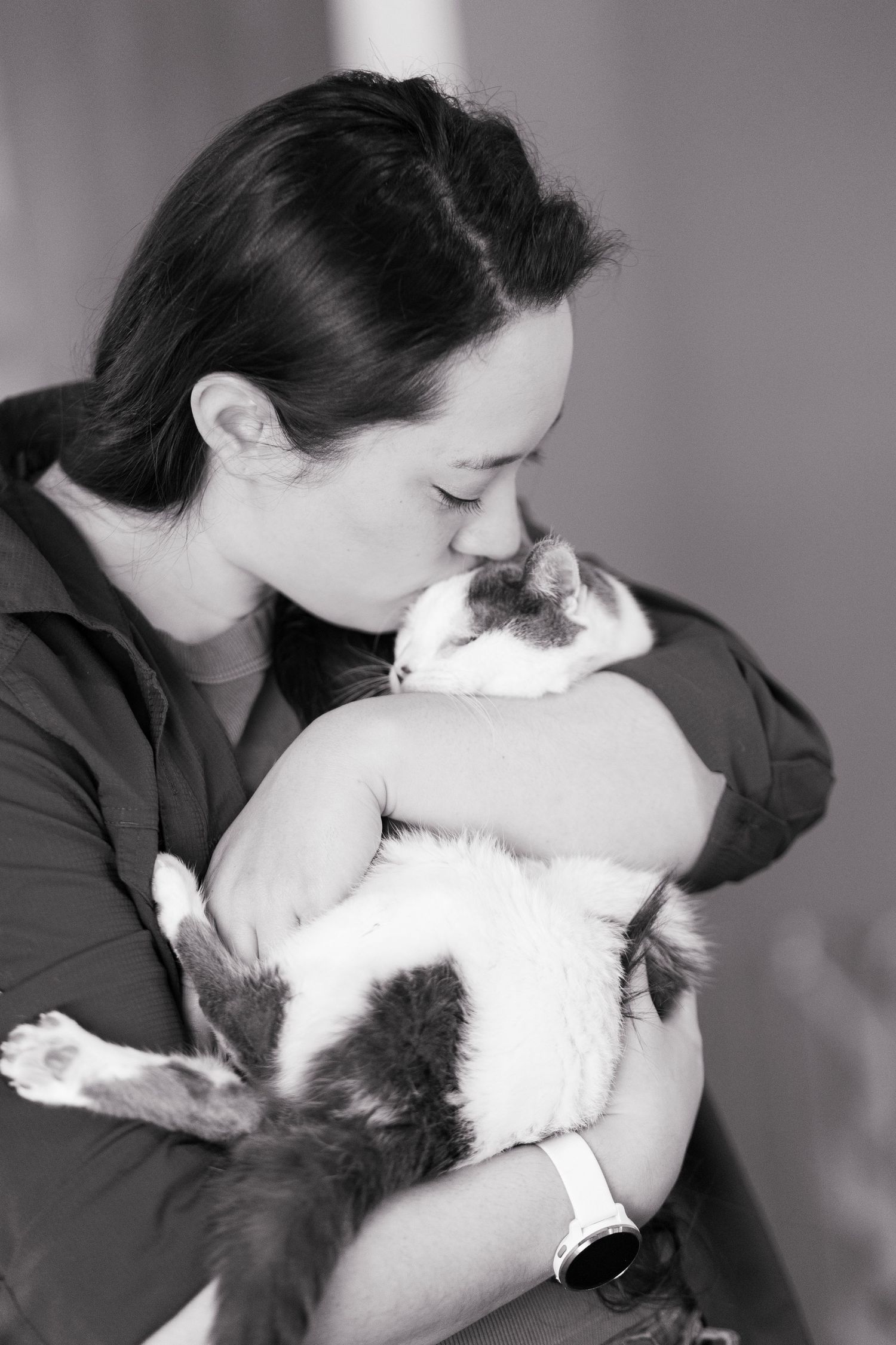 Woman in black shirt kissing her gray and white cat in a black and white portrait photo.