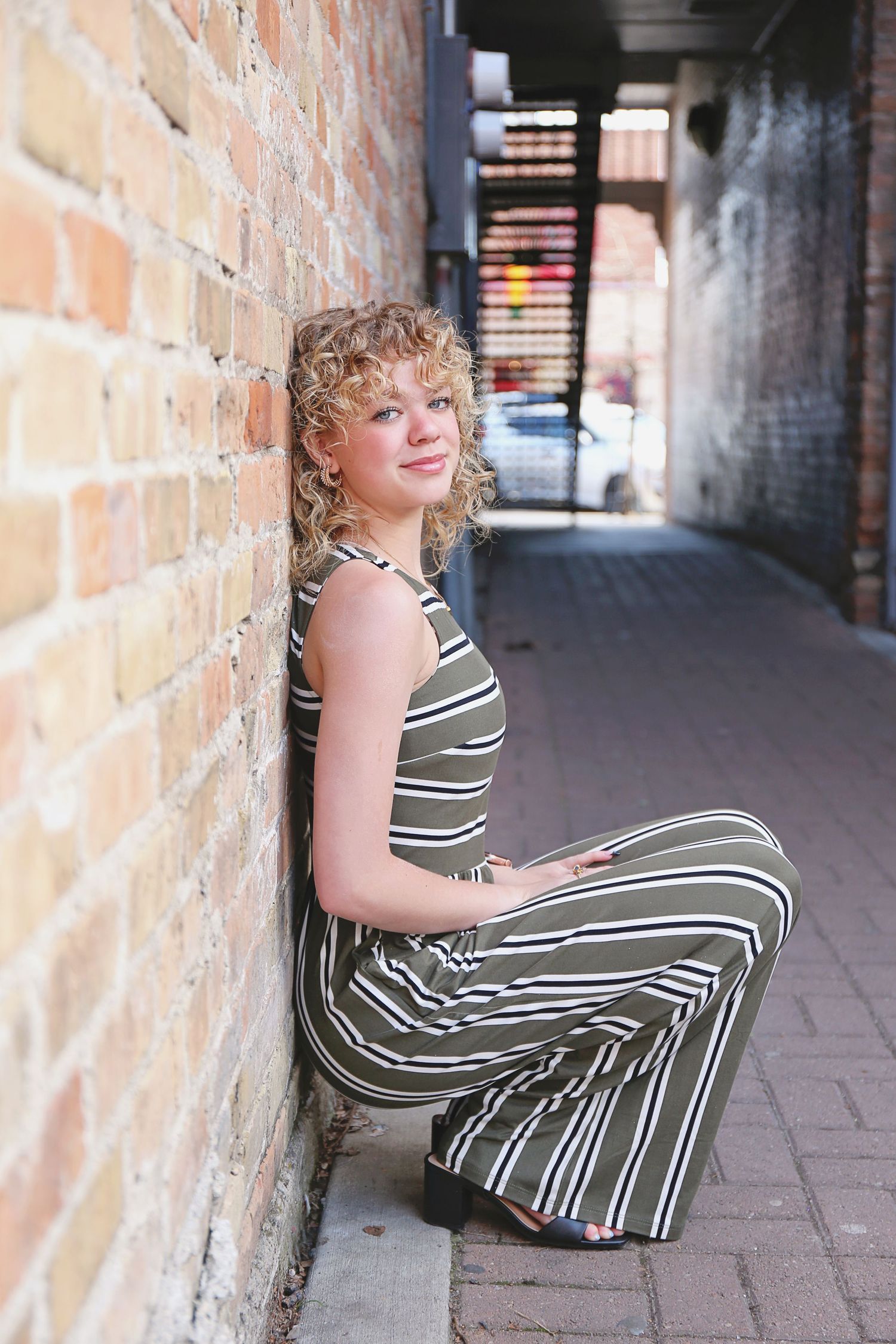 Person in striped dress poses against brick wall in urban setting.