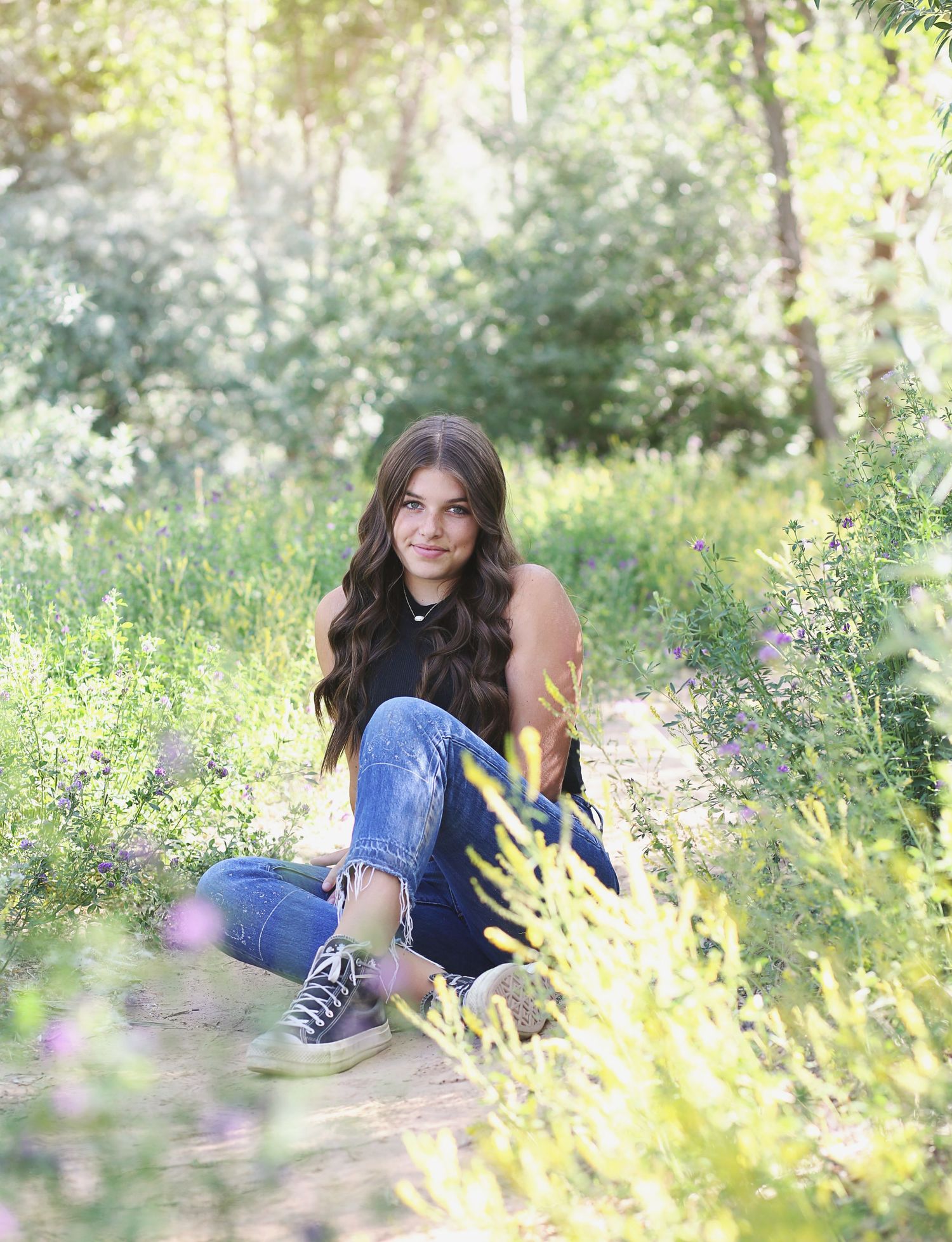 Candid outdoor photography session with someone in denim and dark top sitting among wildflowers.