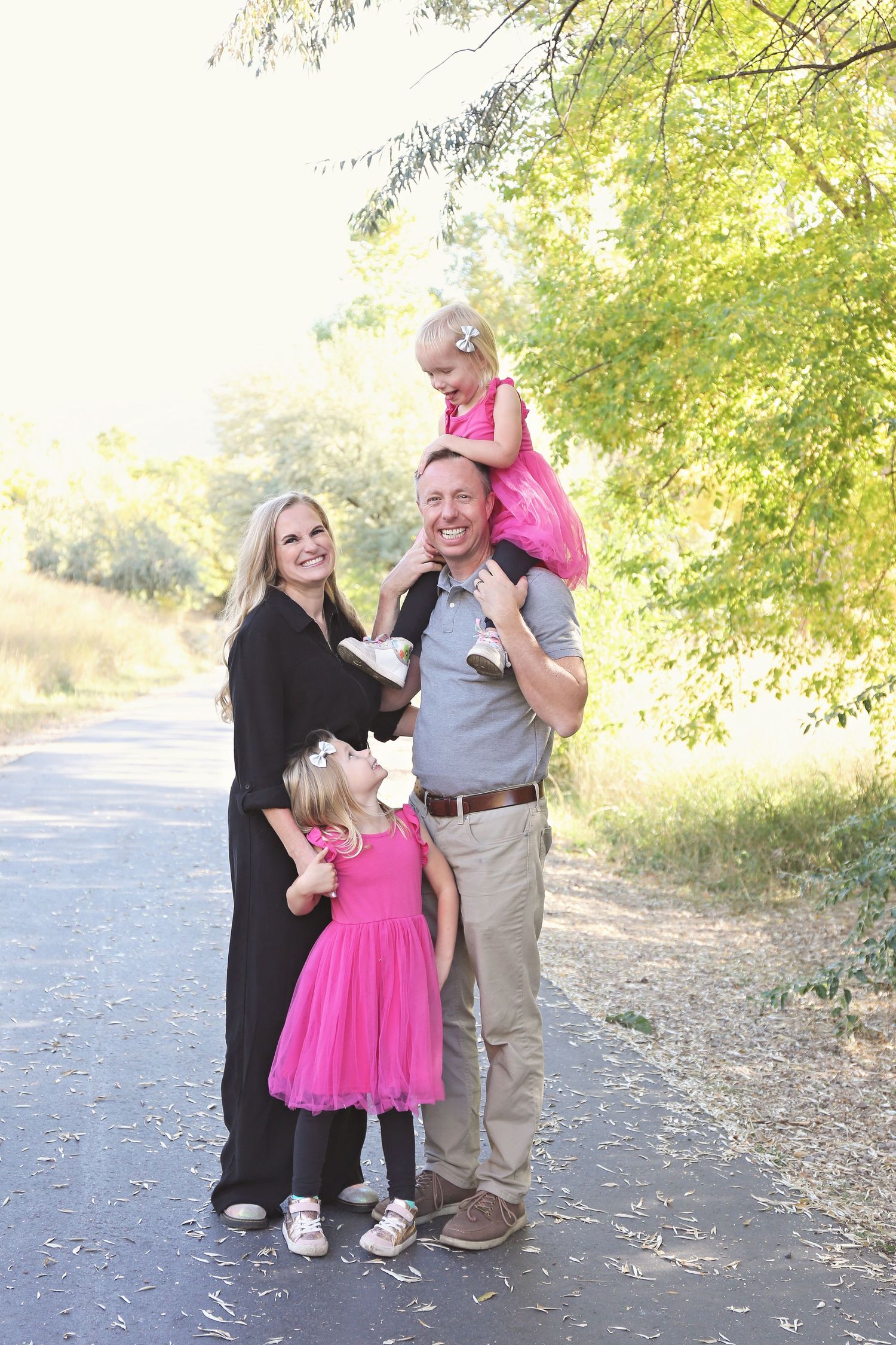 Family in black and pink outfits sharing tender moments on a tree-lined path.
