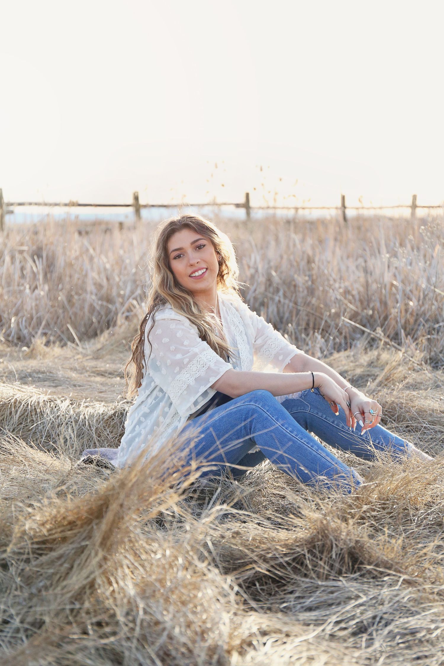 White lace top and jeans ensemble styled in rustic field setting at sunset.