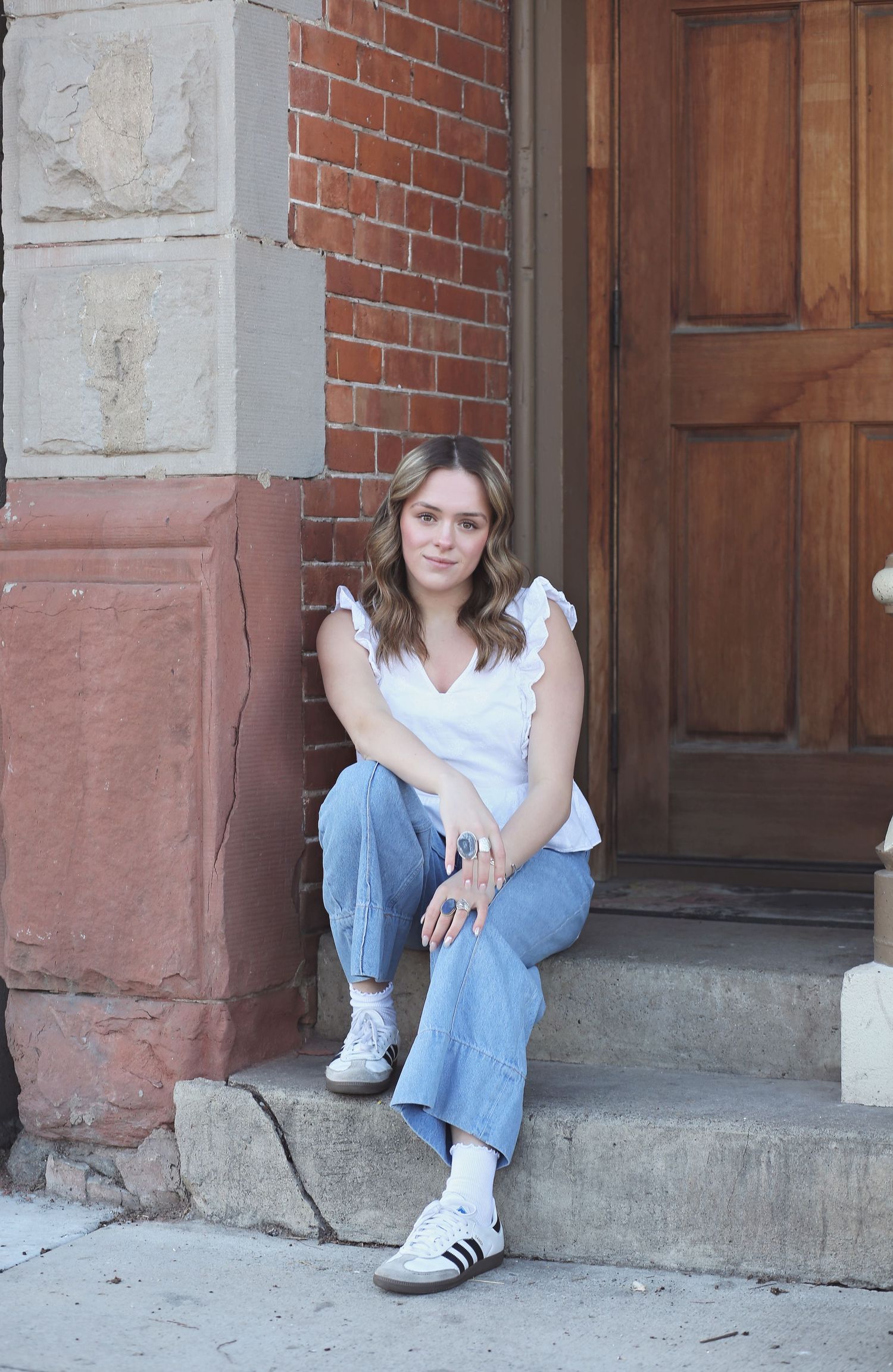 Person sitting on stone steps by a brick building entrance wearing casual denim and white.