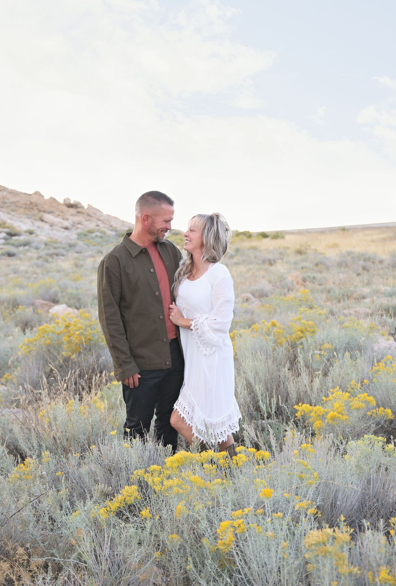 Couple embracing among desert sagebrush and yellow wildflowers at sunset.