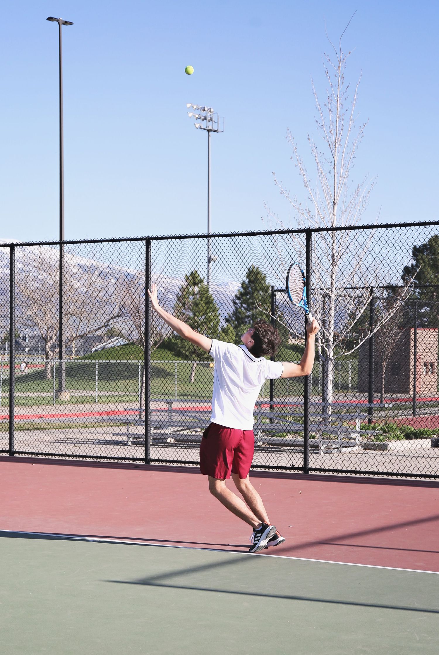 Series of action shots showing tennis player serving on outdoor court with mountains in background.