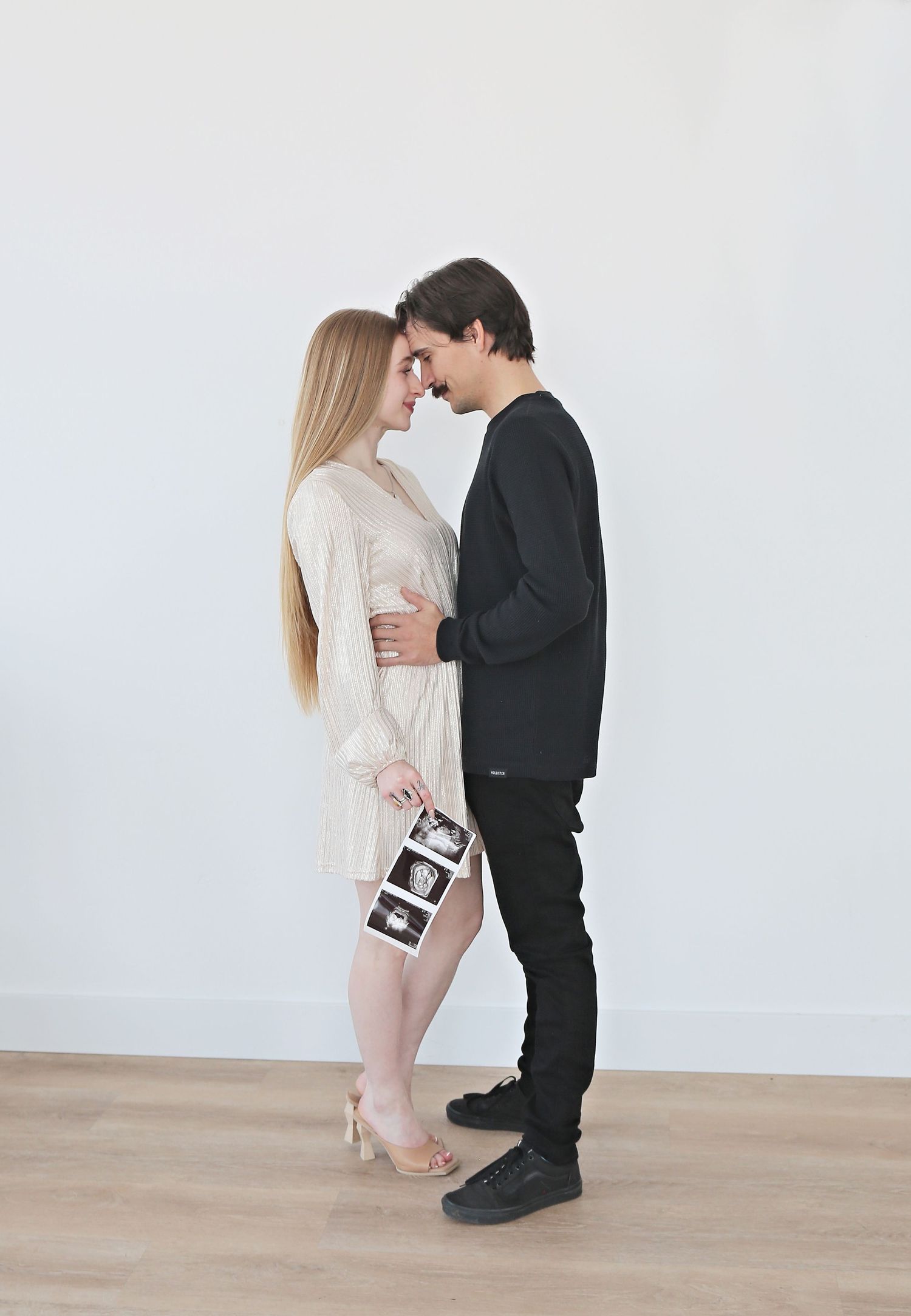 Couple in contrasting outfits share an intimate moment while holding ultrasound photos.