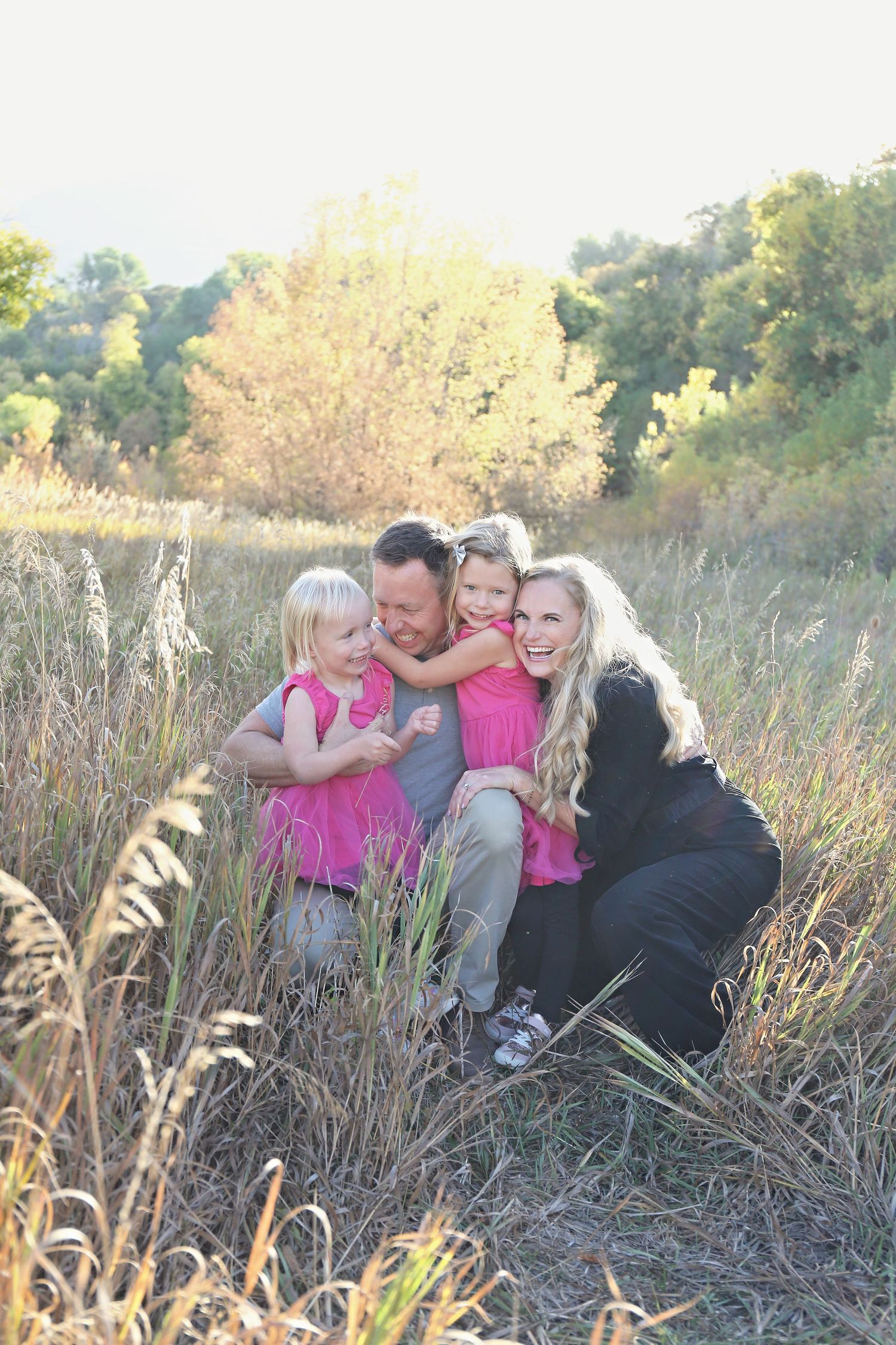 Family group sitting together in tall grass during golden hour sunset photoshoot.