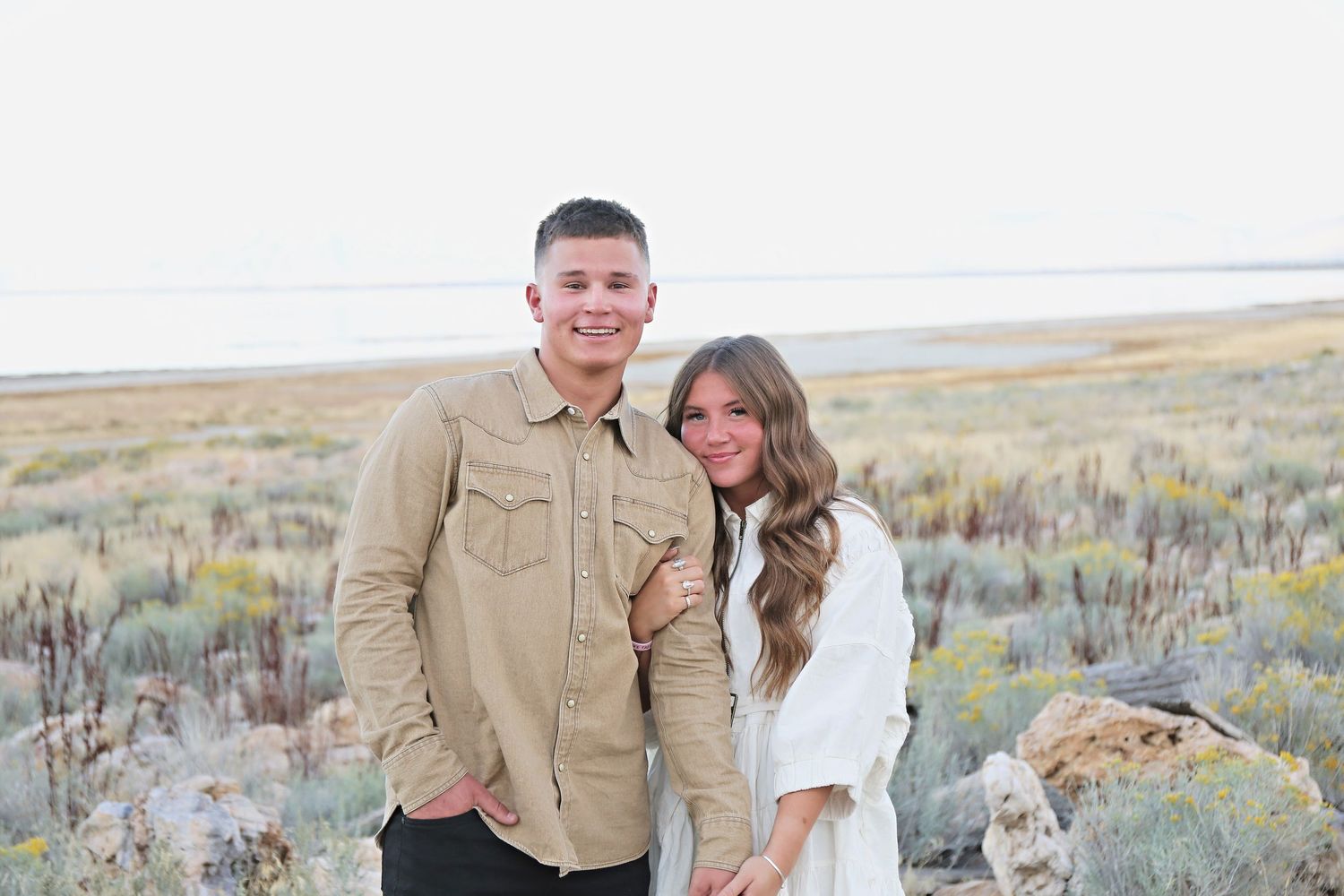 A couple poses together in casual attire against a scenic desert salt flat landscape.