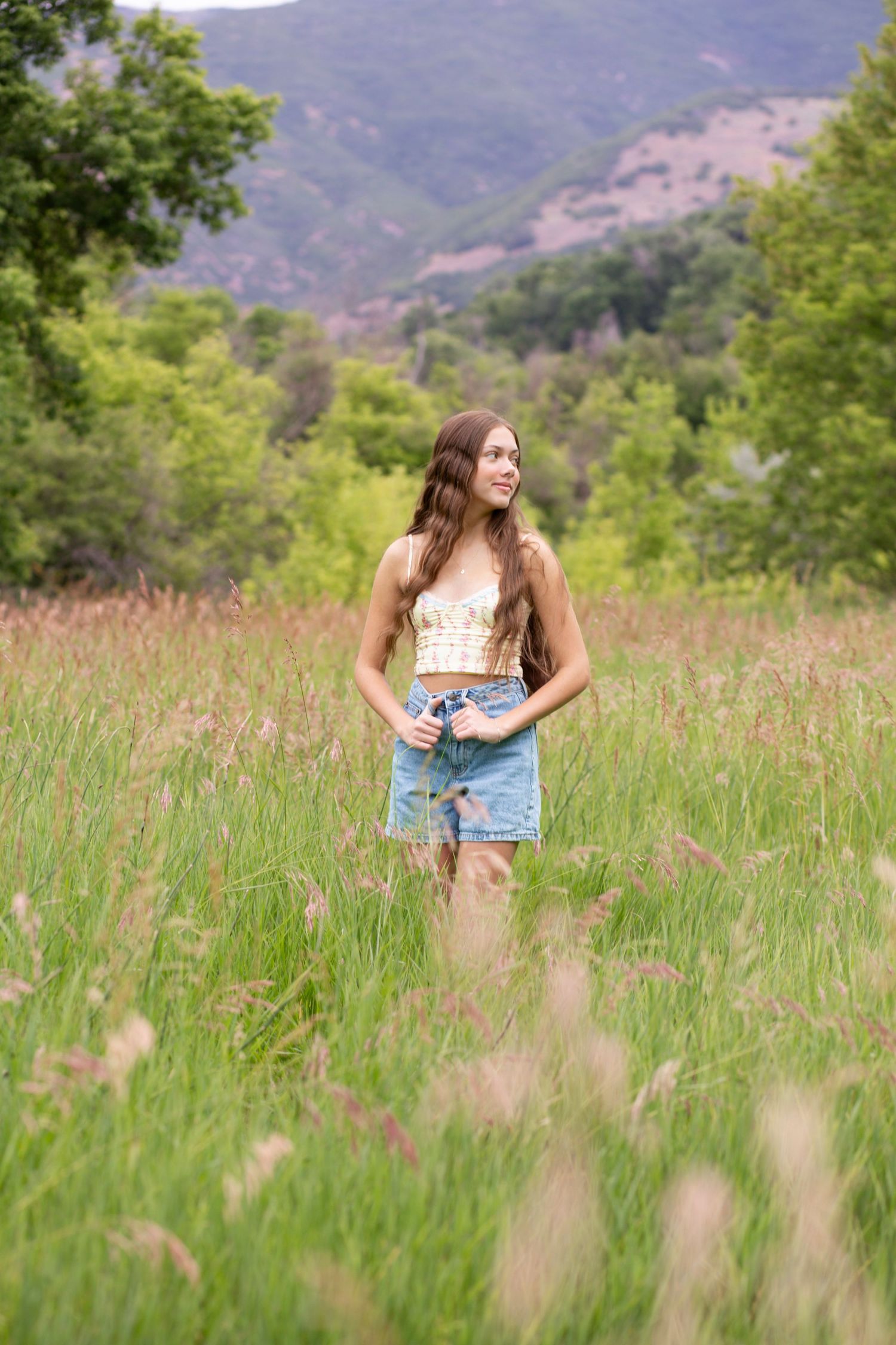 Summer fashion portrait in tall grass meadow with mountains and trees in background.