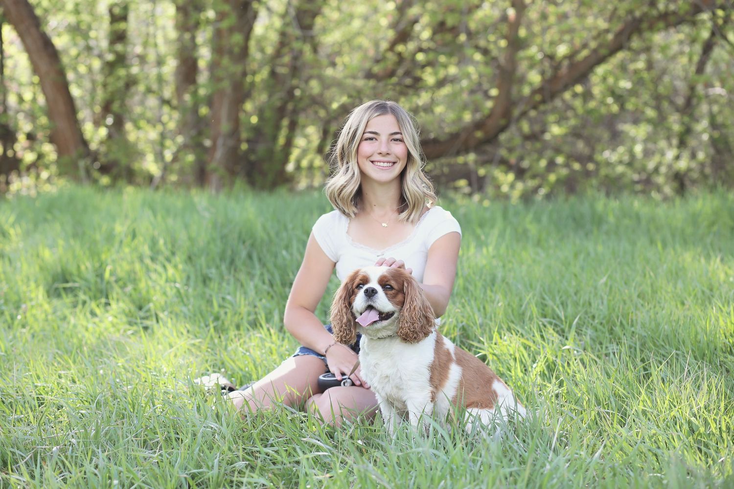 A dog rests on green grass next to someone during an outdoor photoshoot.
