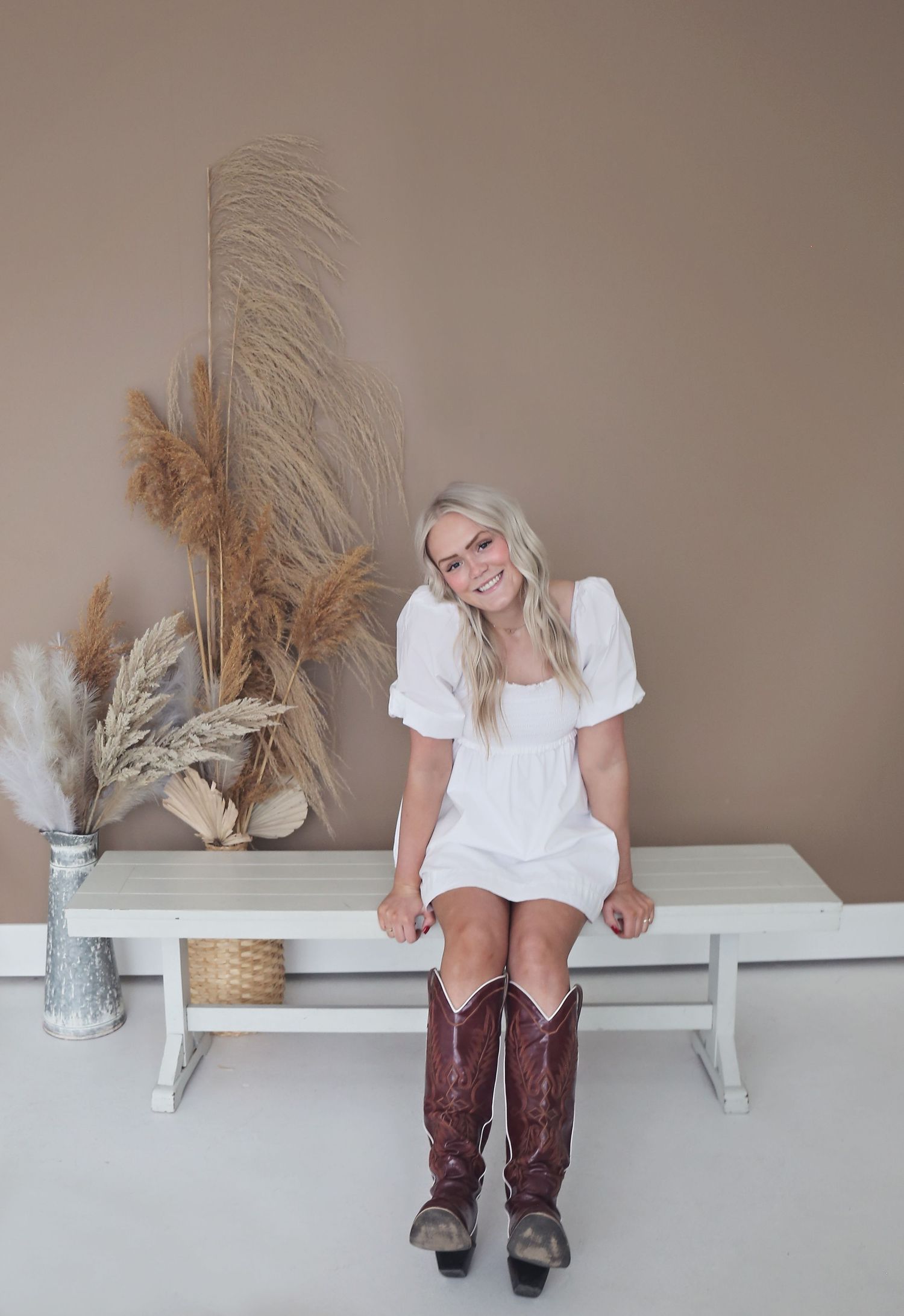 Studio portrait on white bench with dried pampas grass decor and brown cowboy boots.
