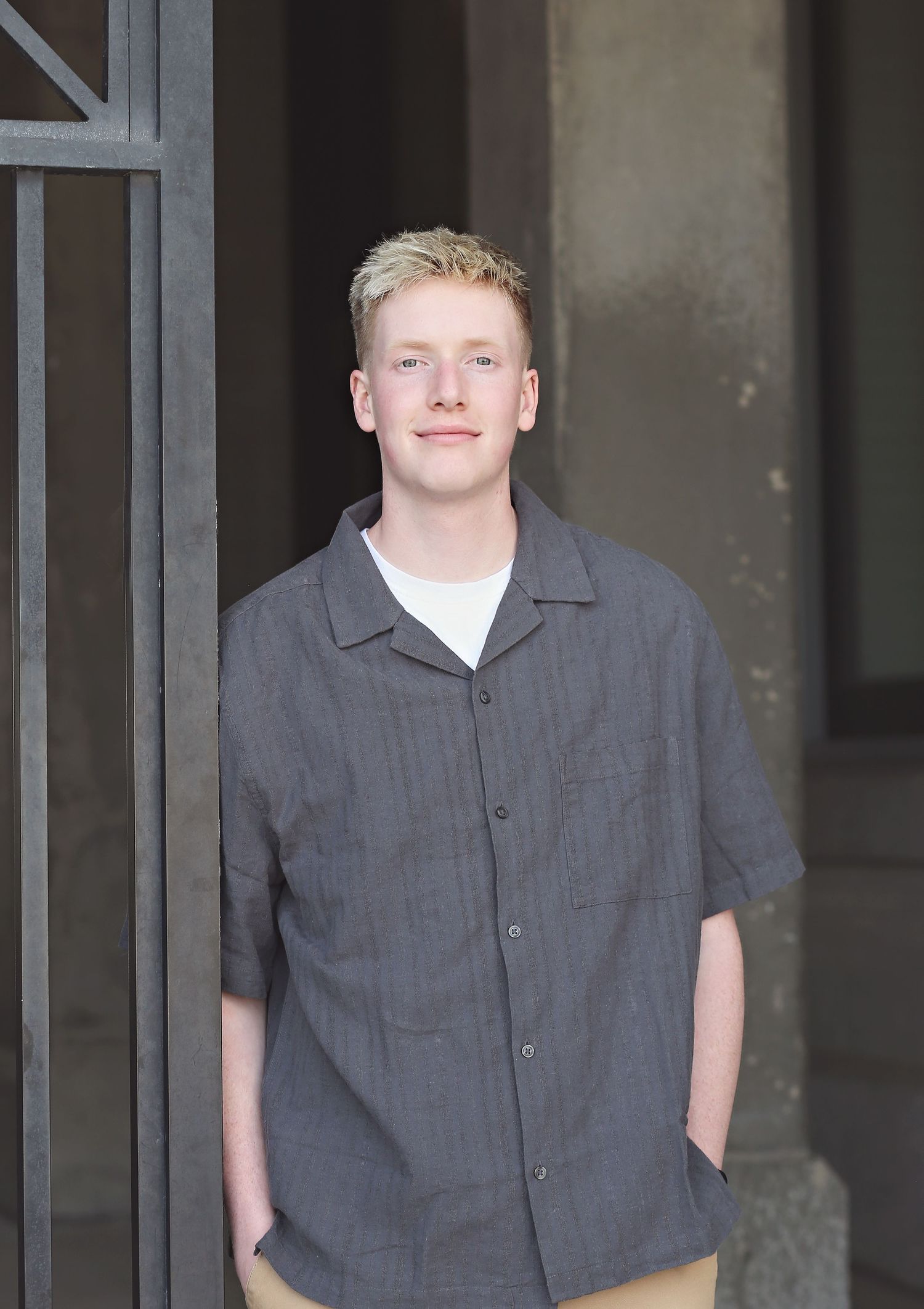 Casual portraits in a grey button-up shirt against a stone column background.