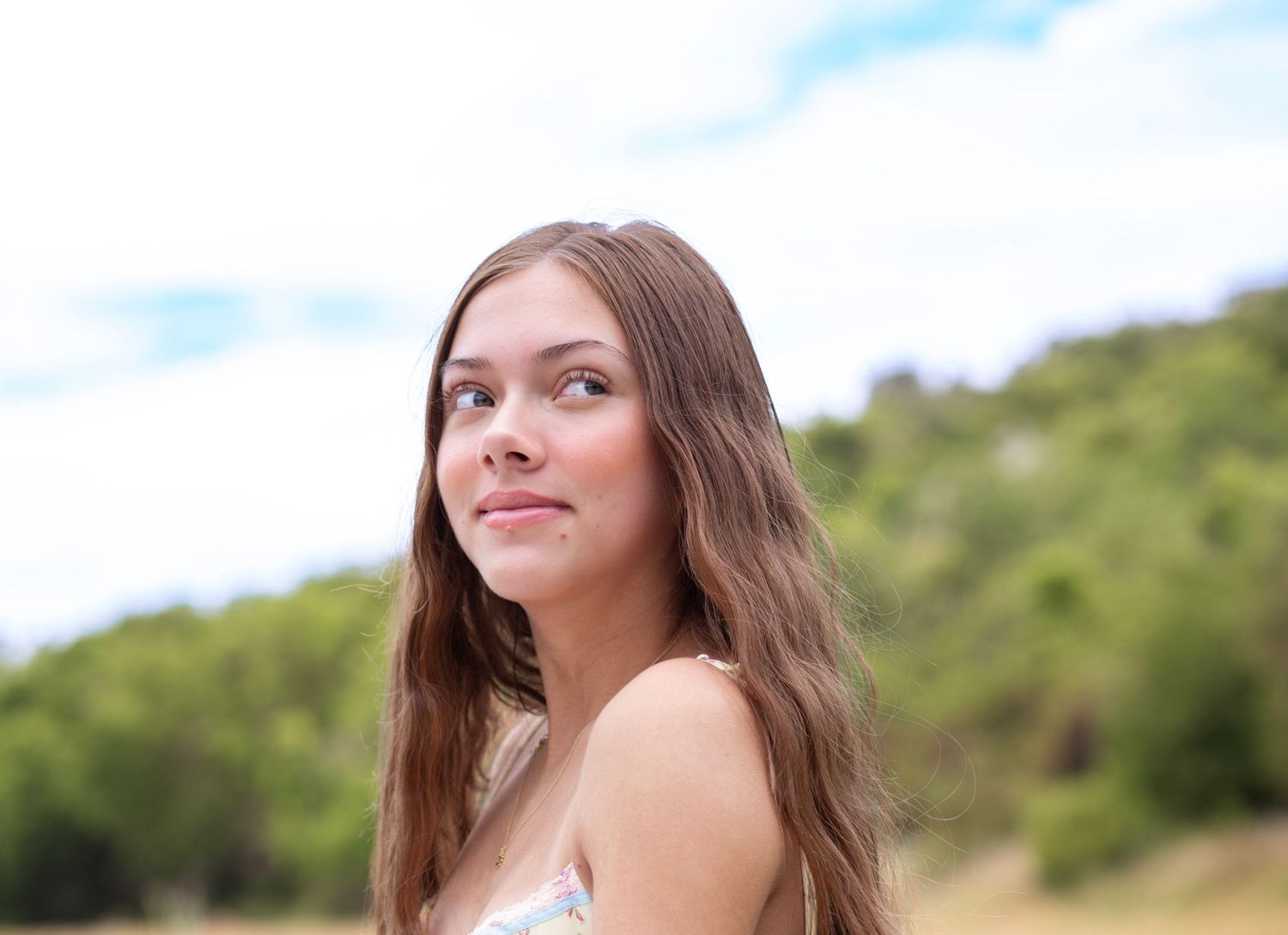 Summer outdoor portrait with natural lighting against blurred hillside background.