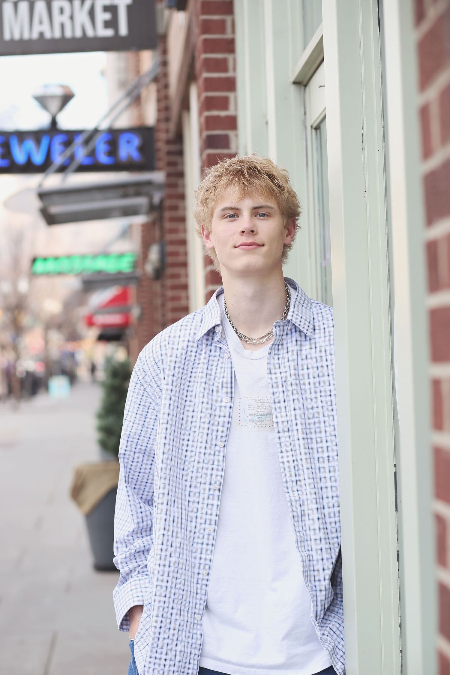 A casual portrait near a storefront wearing a checkered shirt and white t-shirt.