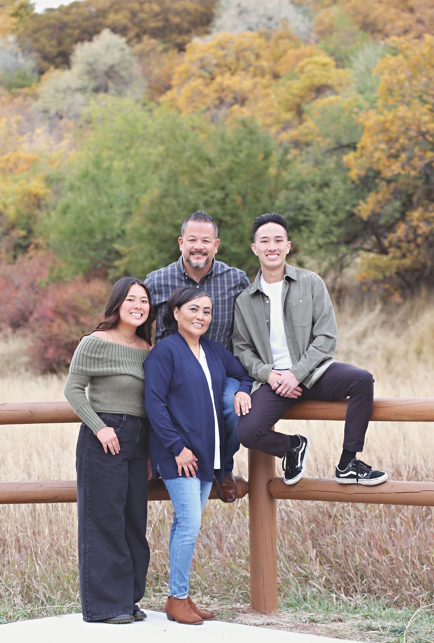 Casual group photo of people sitting and leaning on wooden fence with fall colors in background.
