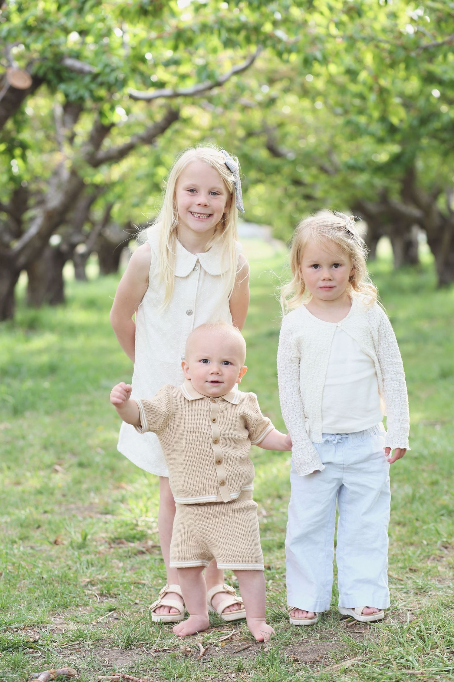 Young children standing together in light colored outfits on grass.