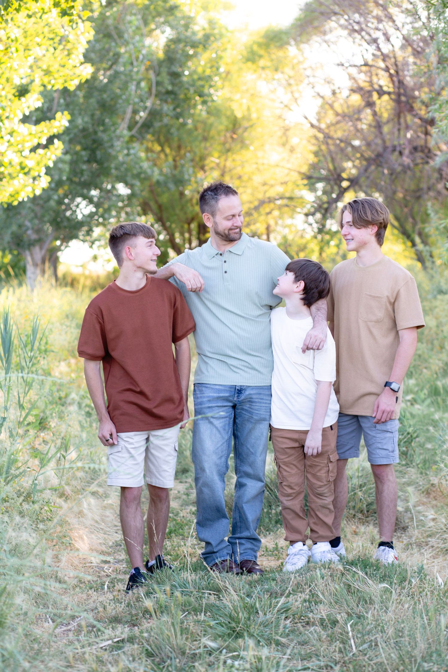 Family group poses together in a natural outdoor setting with tall grass and golden sunlight.