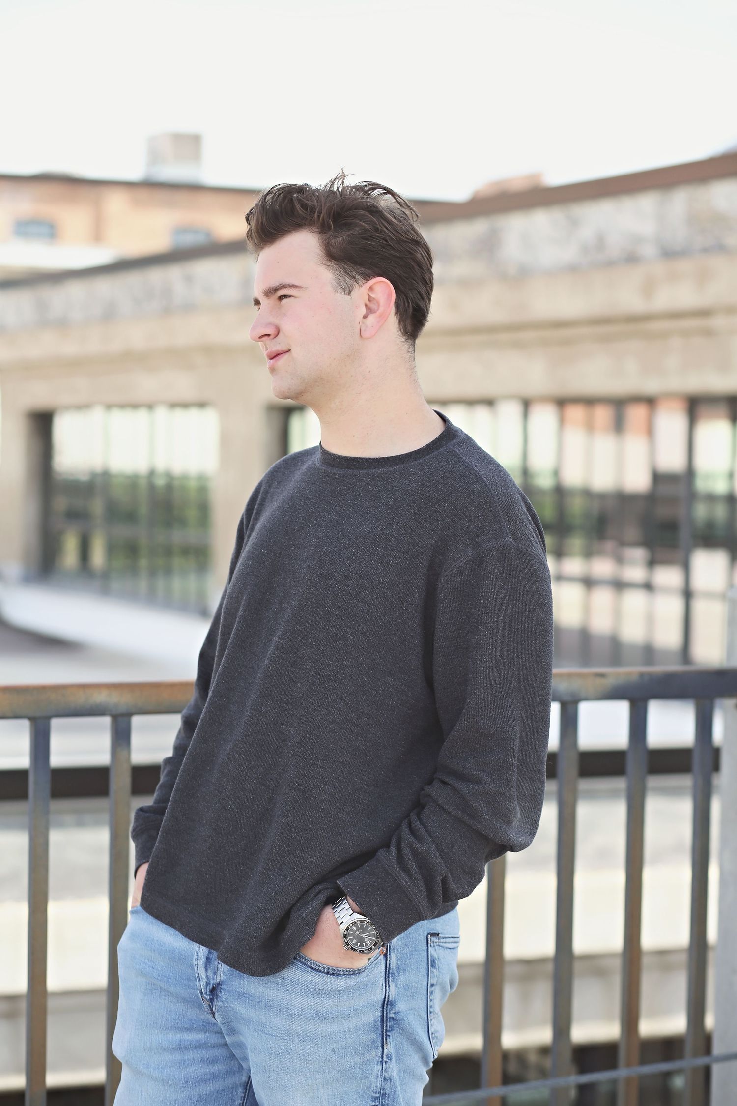 Urban portrait of person in dark sweater and jeans against industrial building backdrop.