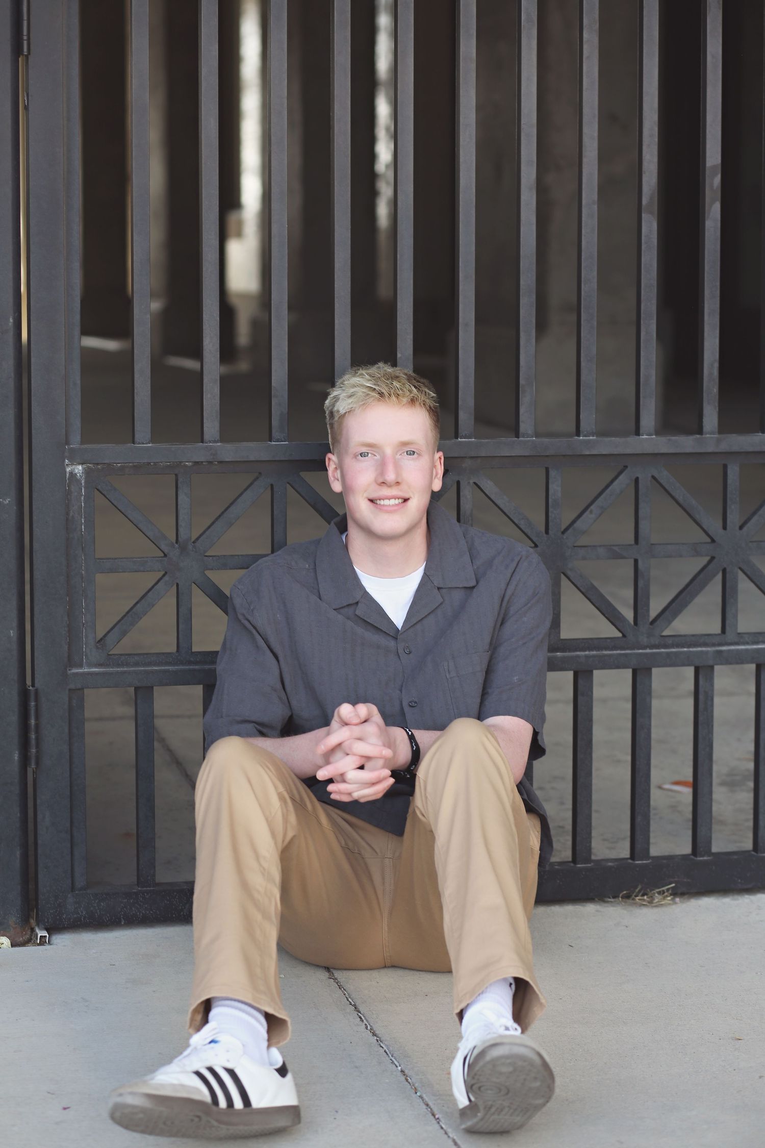 Person in casual attire sits on concrete steps near metal gate.