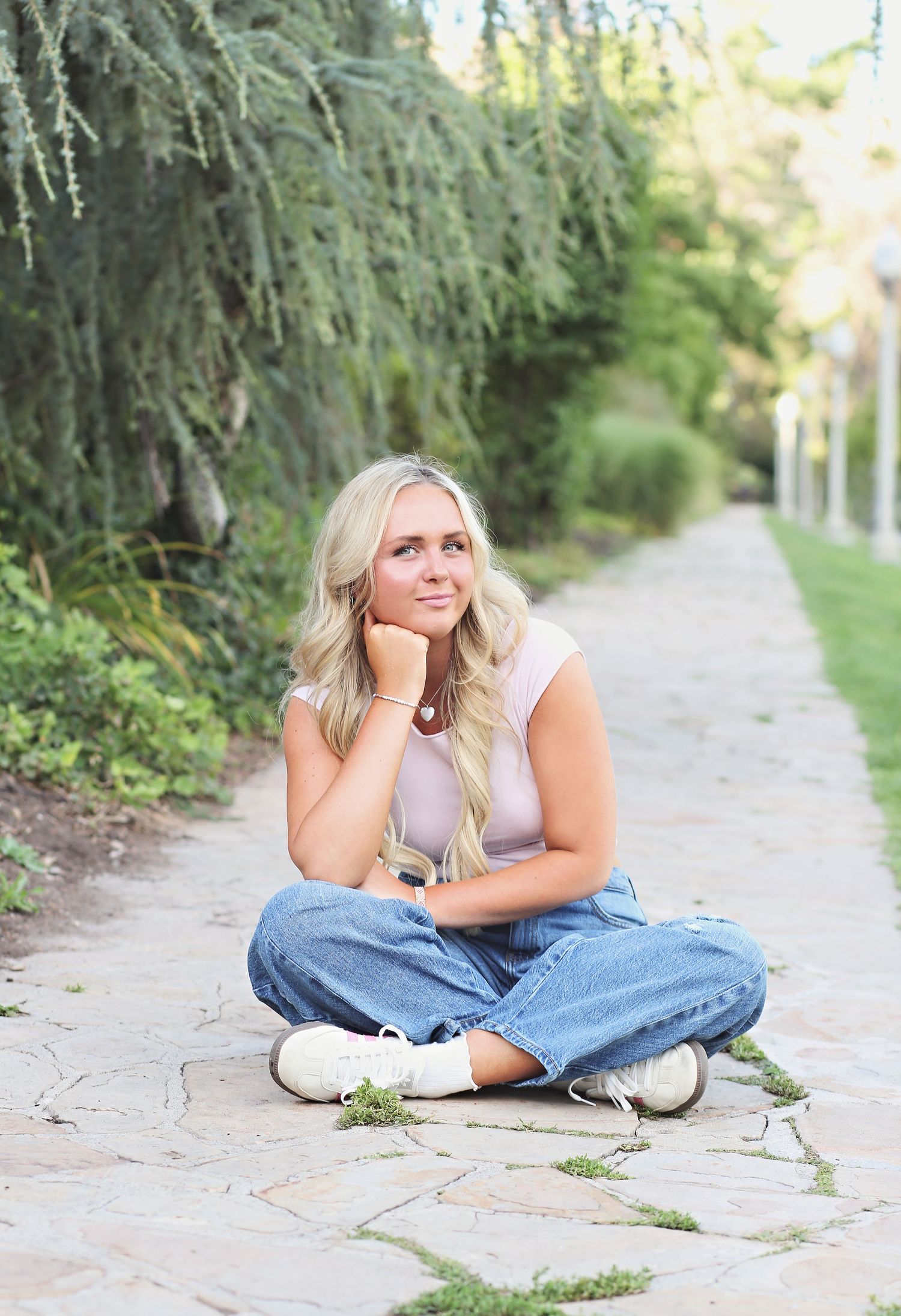 A casual outdoor portrait on a stone path with lush greenery in the background.