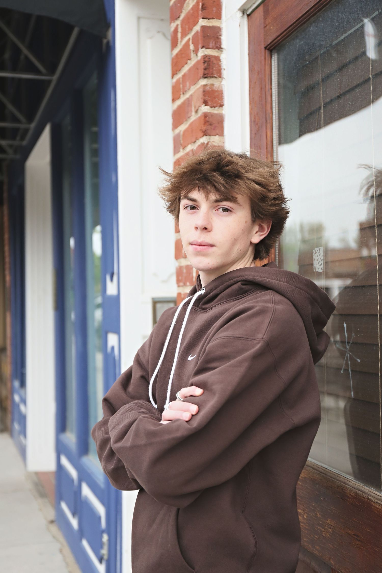 Person in brown hoodie poses against brick wall with blue trim in multiple casual shots.