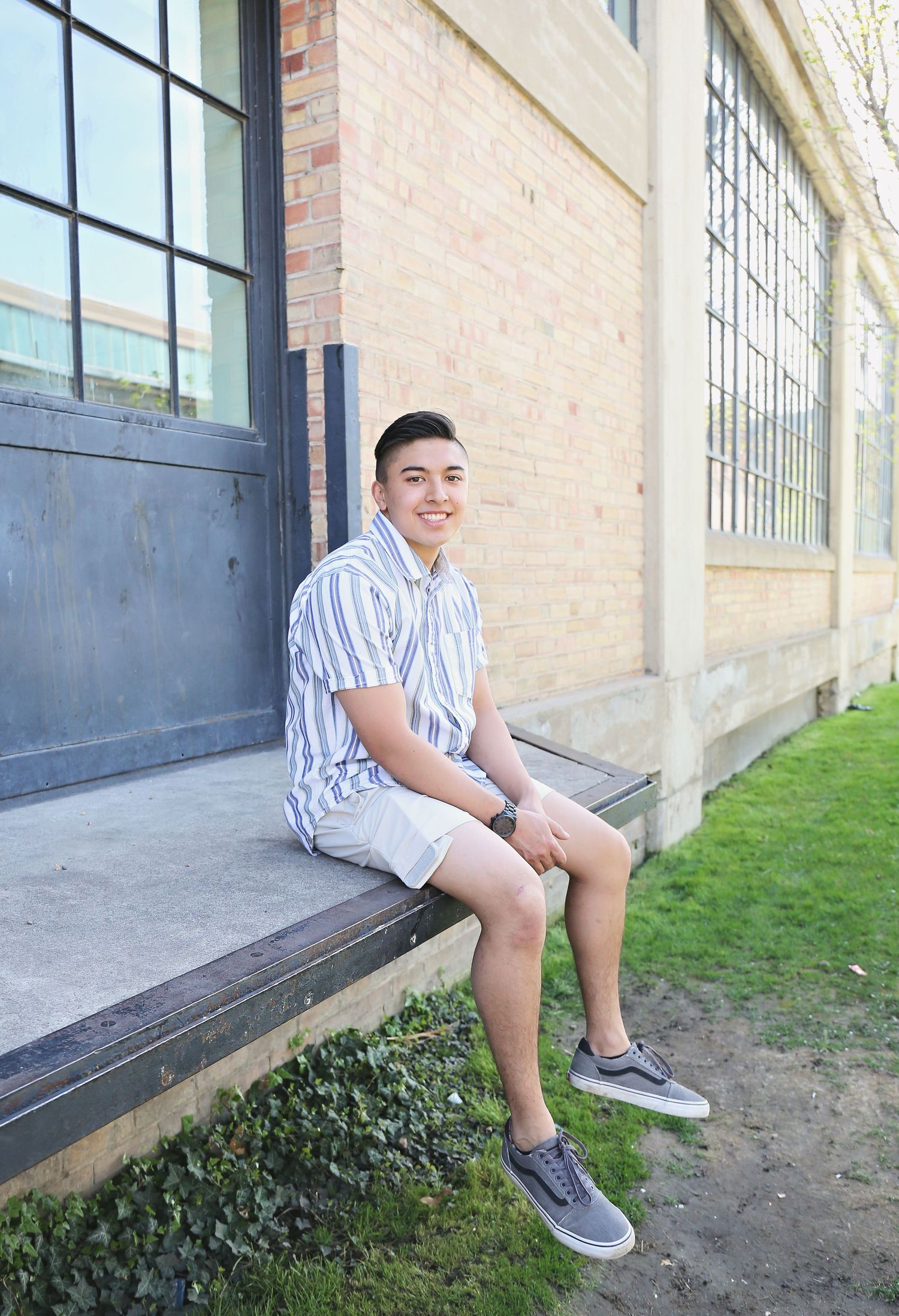 Person in striped shirt sitting on a brick building ledge outdoors.