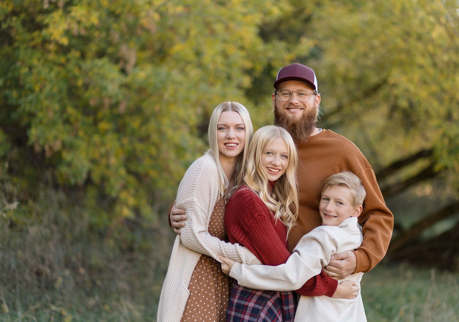 Family group photo session outdoors with autumn trees and natural lighting.