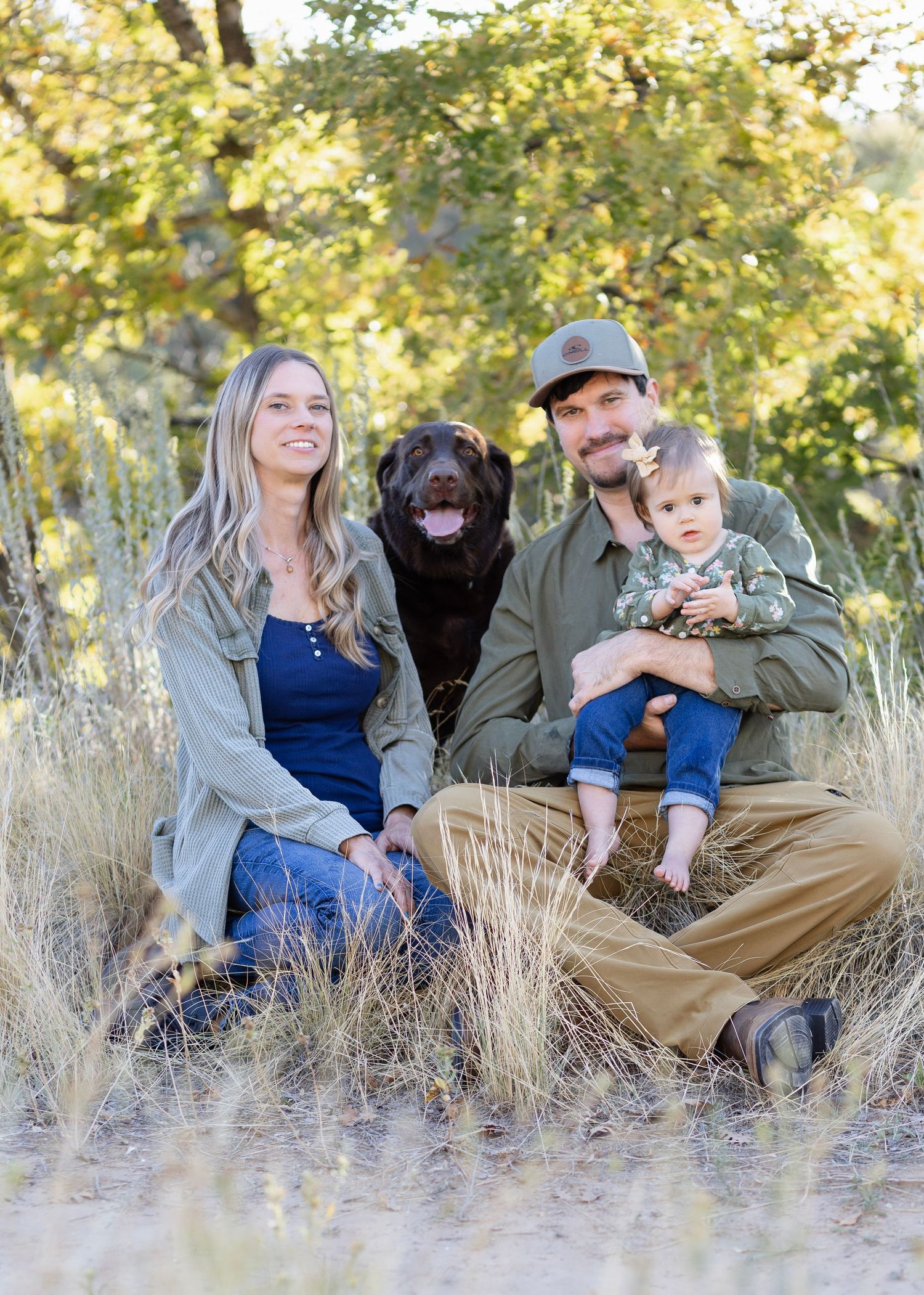 A family relaxes together in tall golden grass during an outdoor autumn photoshoot.