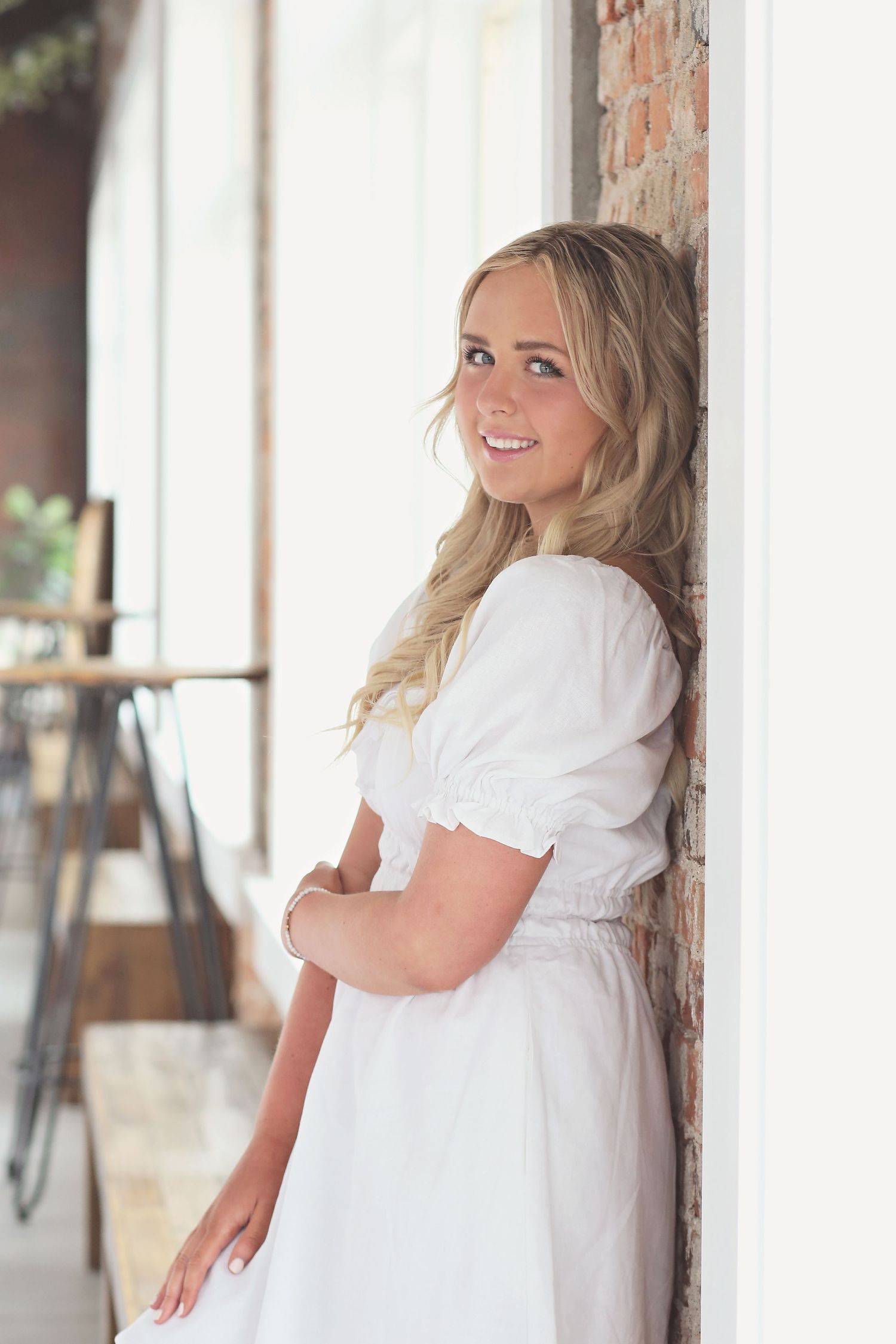 A figure in a flowing white dress poses against a rustic brick wall in a series of candid portrait shots.