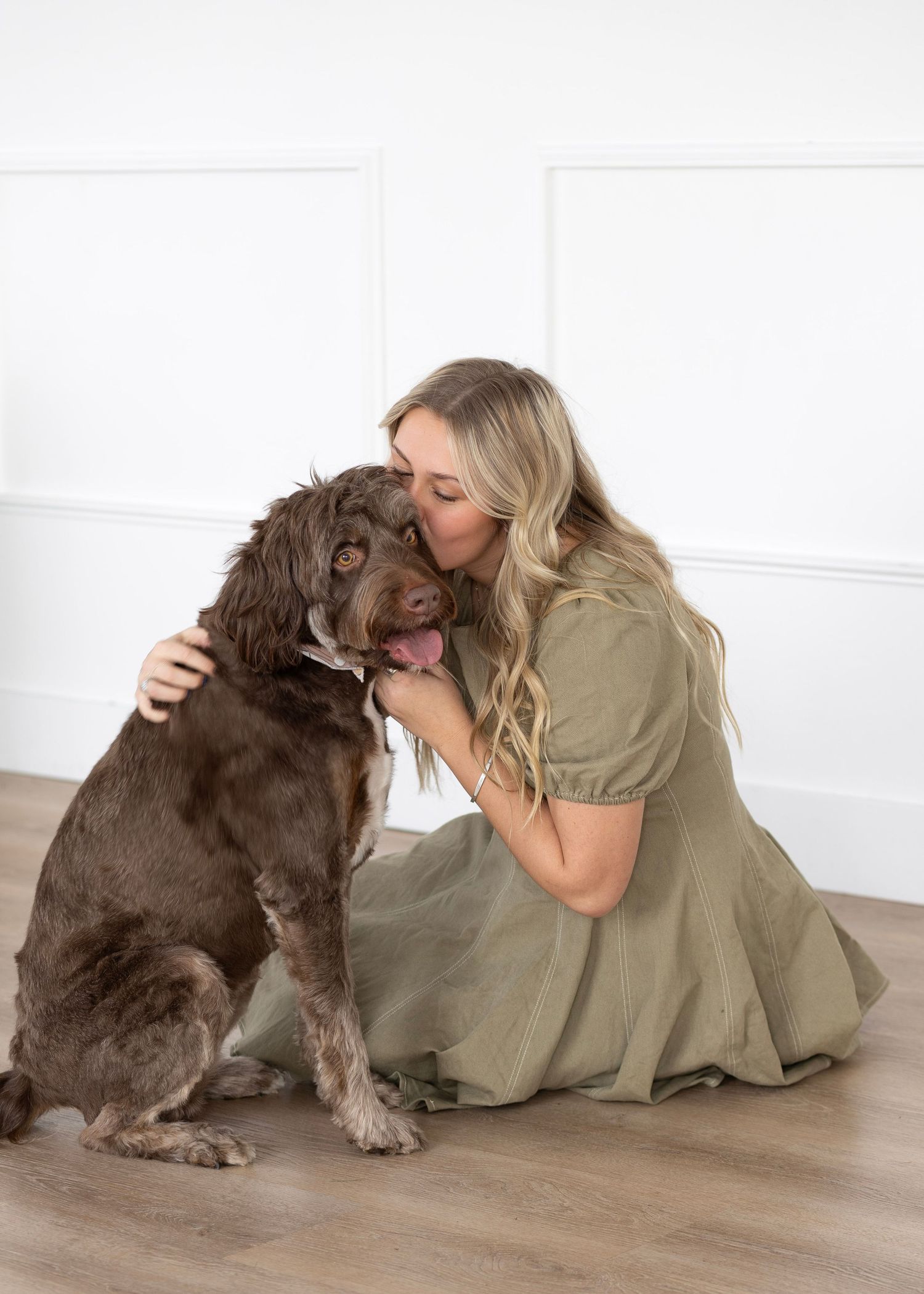 A chocolate-colored dog receives affection while sitting on wooden flooring.