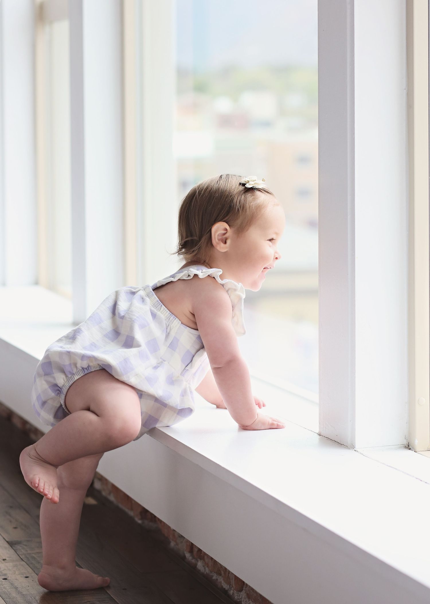 Baby in white outfit crawling and exploring along a sunny window ledge.