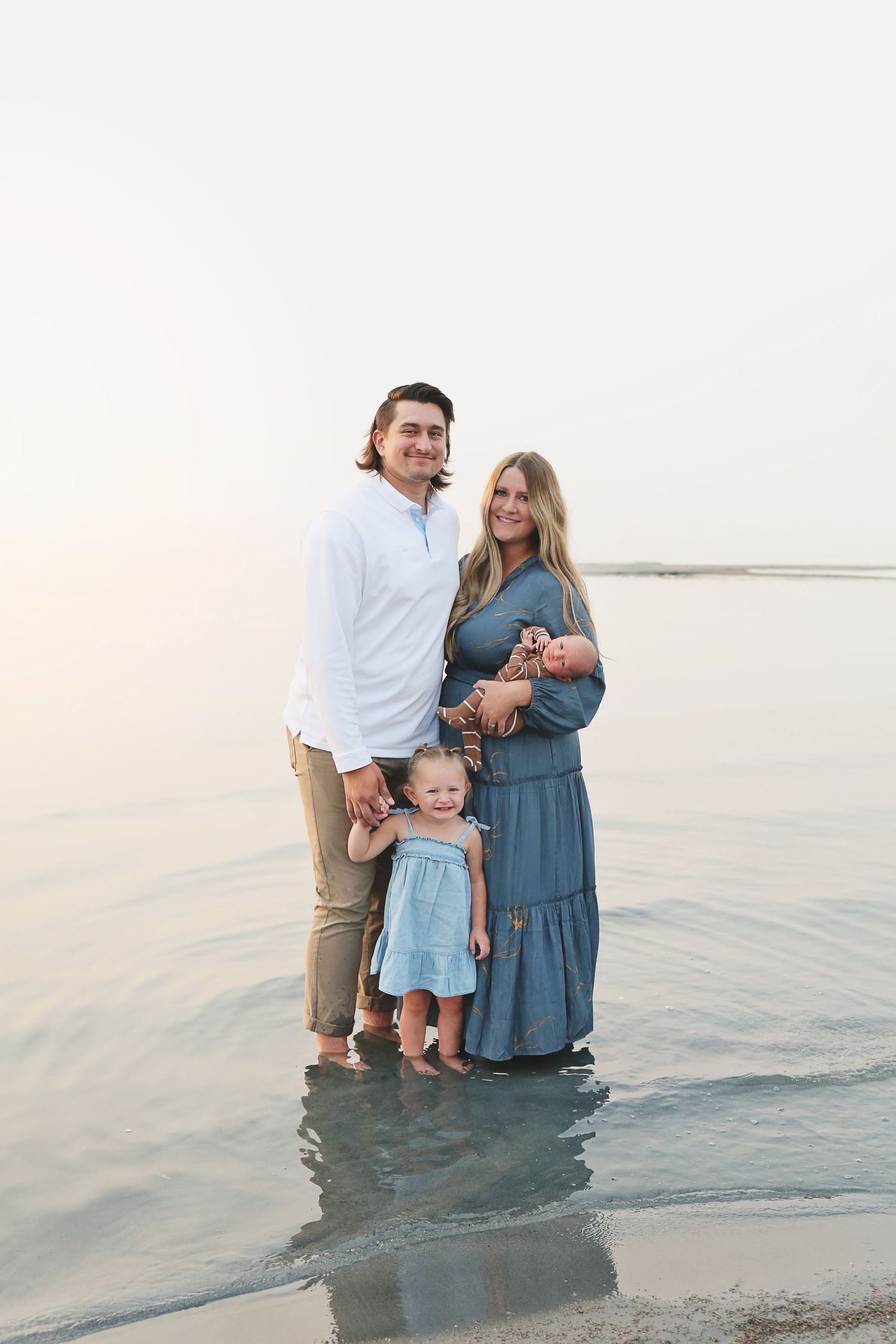 A family standing together in shallow ocean water during golden hour.