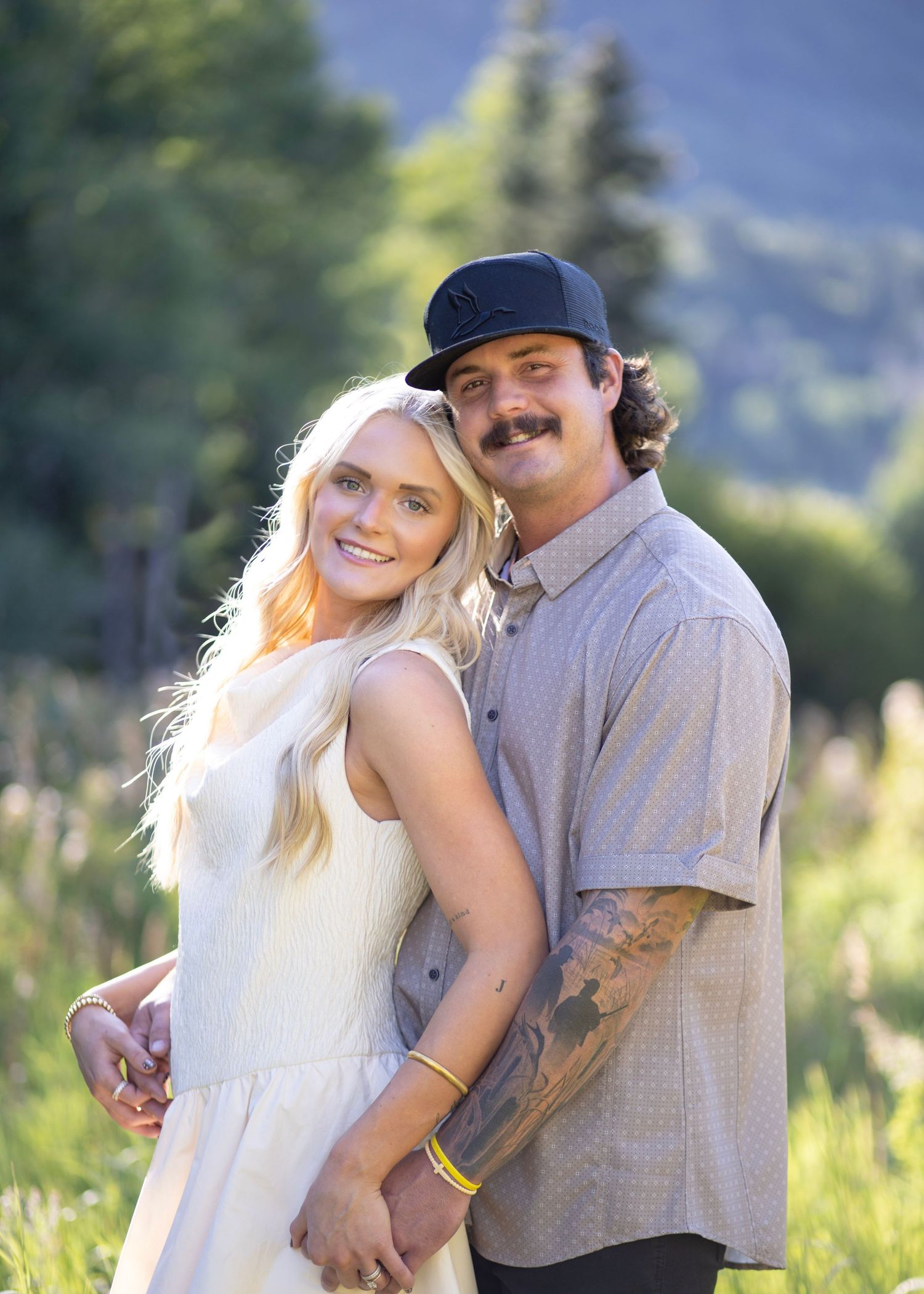 Couple sharing tender moments in a sunlit field with mountains in the background.
