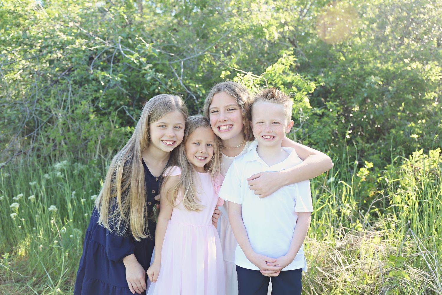 Family photo session in a lush green outdoor setting with natural sunlight filtering through trees.