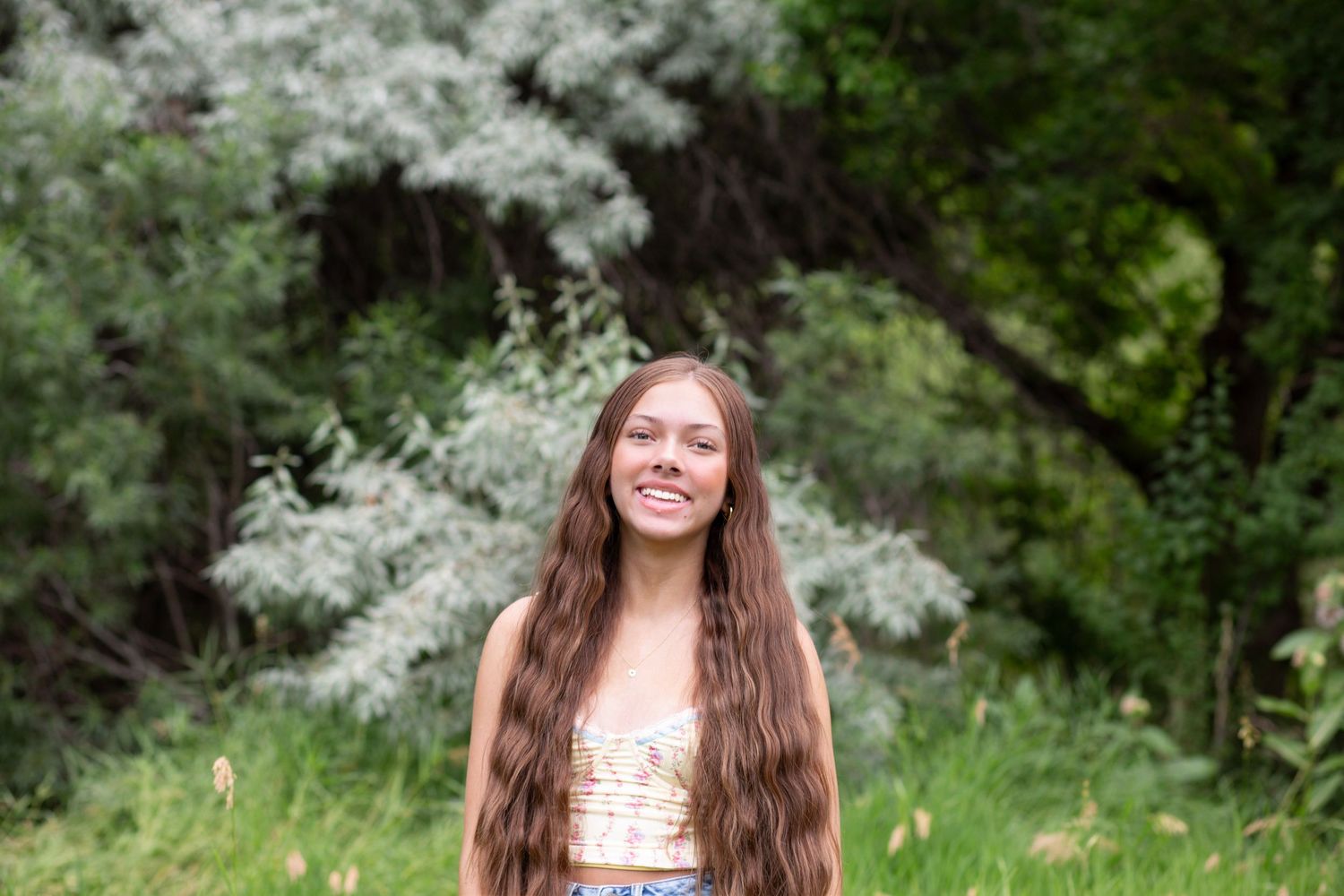 Natural outdoor portrait with flowing long hair against white flowering trees and green foliage.