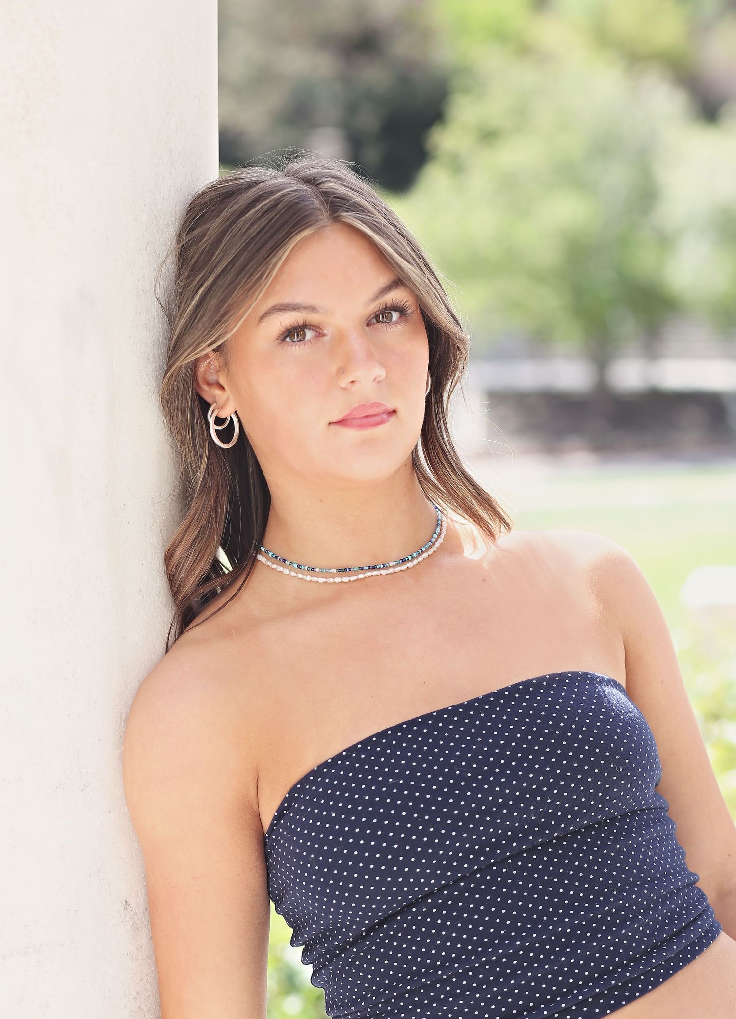 Close-up portrait showcasing a navy polka dot top and silver necklace in natural lighting.