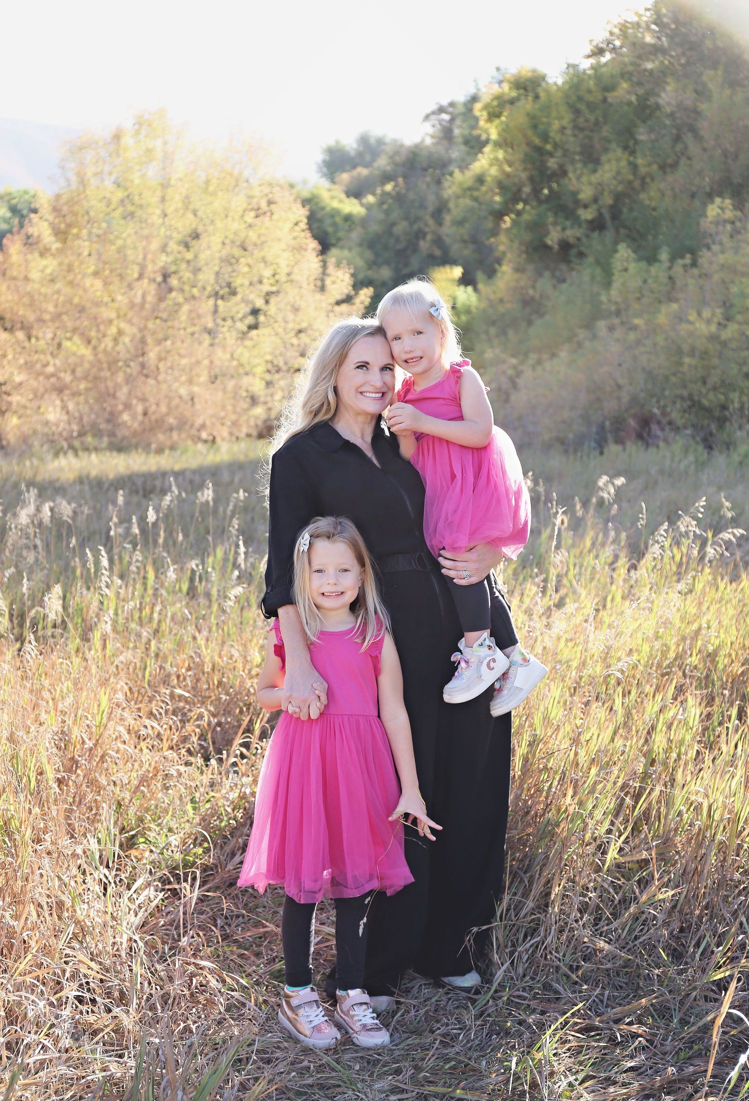 Family portrait in black and pink clothing against tall grass in natural lighting.