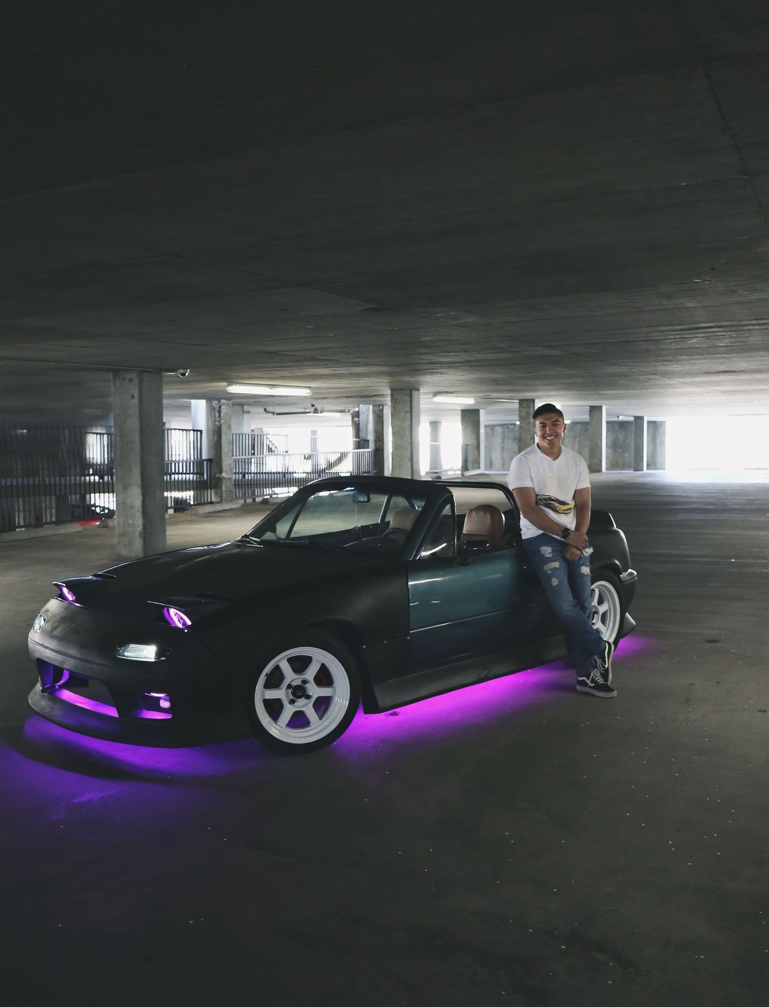 Black car with purple LED underglow lighting in dark parking garage.