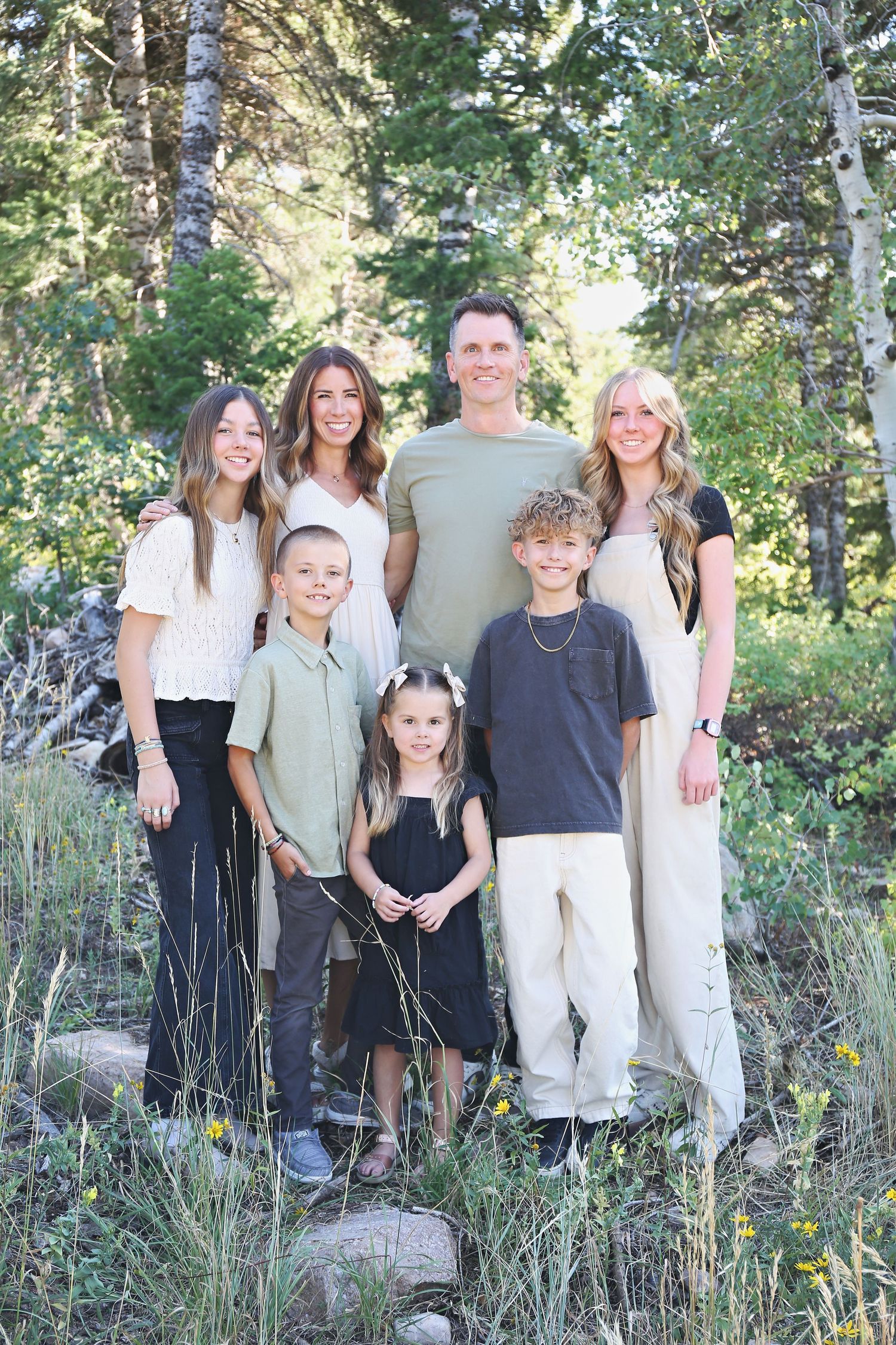 Family of seven poses together outdoors in coordinated neutral outfits among aspen trees.