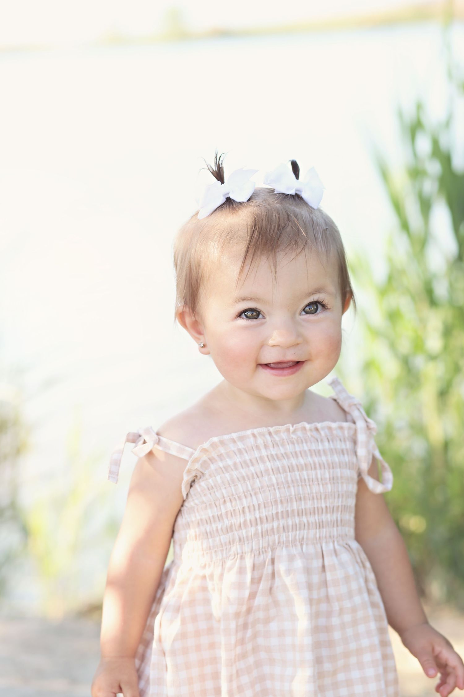 Sweet baby in pink gingham dress with white bow playing outdoors.